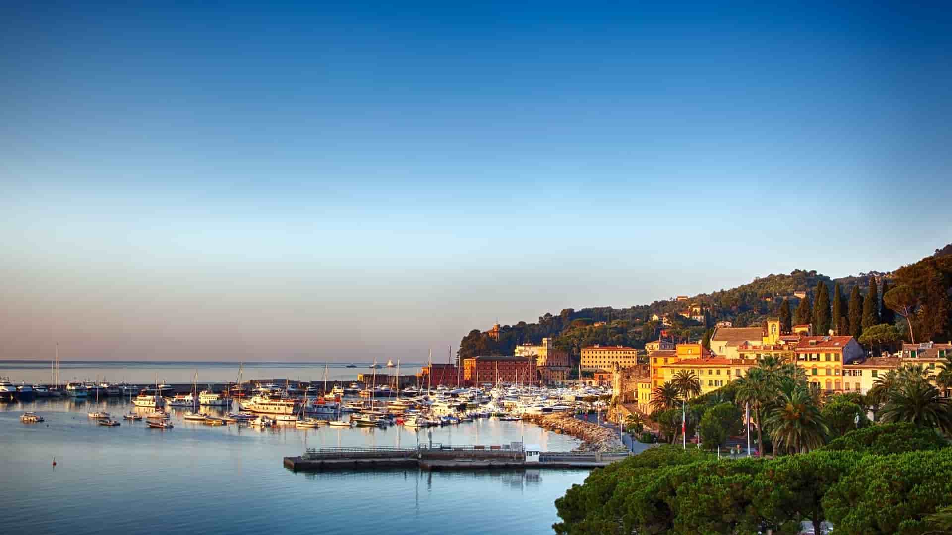 A stunning wide-angle view of the scenic harbor of Santa Margherita Ligure, Italy, with numerous yachts and fishing boats docked against the backdrop of a charming coastal town nestled on a green hillside.