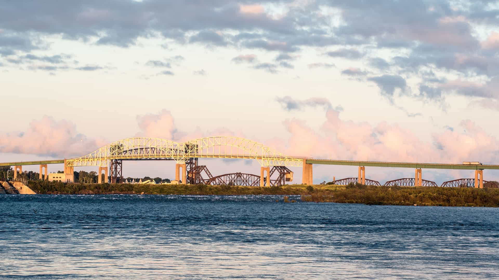 A view of the International Bridge connecting Sault Ste. Marie, Michigan, and Sault Ste. Marie, Ontario, over the St. Mary's River with a cloudy evening sky.