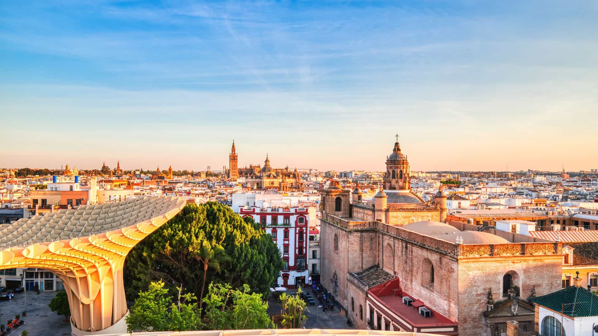 A scenic view of the iconic Plaza de EspaƱa in Seville, Spain, featuring its grand arcade of arches and columns, a main building with a clock tower, and a bright blue sky.