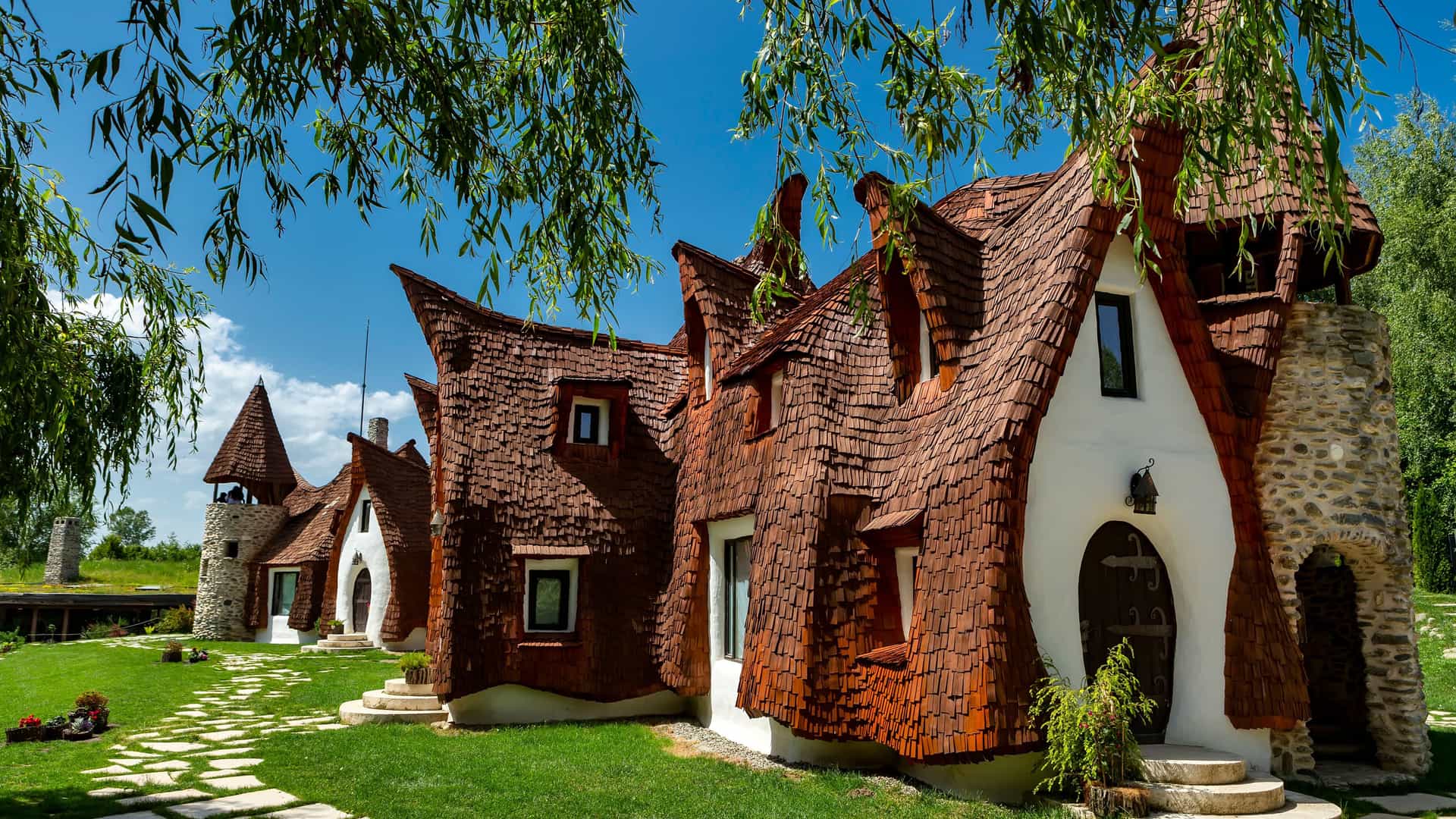 "A unique view of the ""Clay Castle of the Valley of Fairies"" in Porumbacu de Sus, Romania, near Sibiu, with its distinctive hobbit-style architecture and whimsical thatched roof. "
