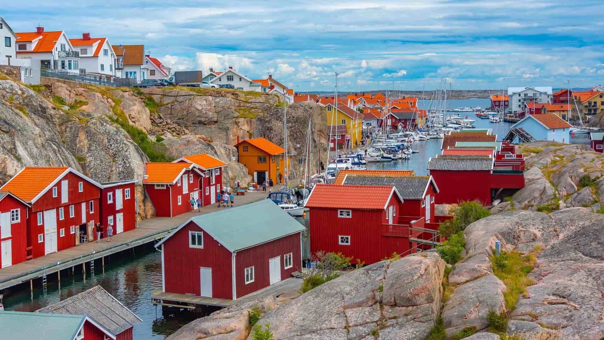 A stunning view of the Skagerrak Strait coastline, with a picturesque fishing village of colorful red houses nestled among the rocky shoreline and a harbor full of boats.