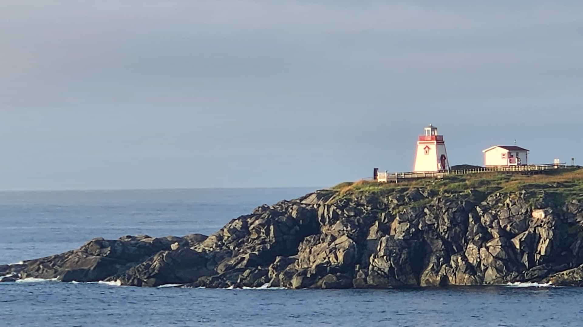 A picturesque view of a red and white lighthouse on a rocky cliff overlooking the vast Atlantic Ocean in St. Anthony, Newfoundland and Labrador.