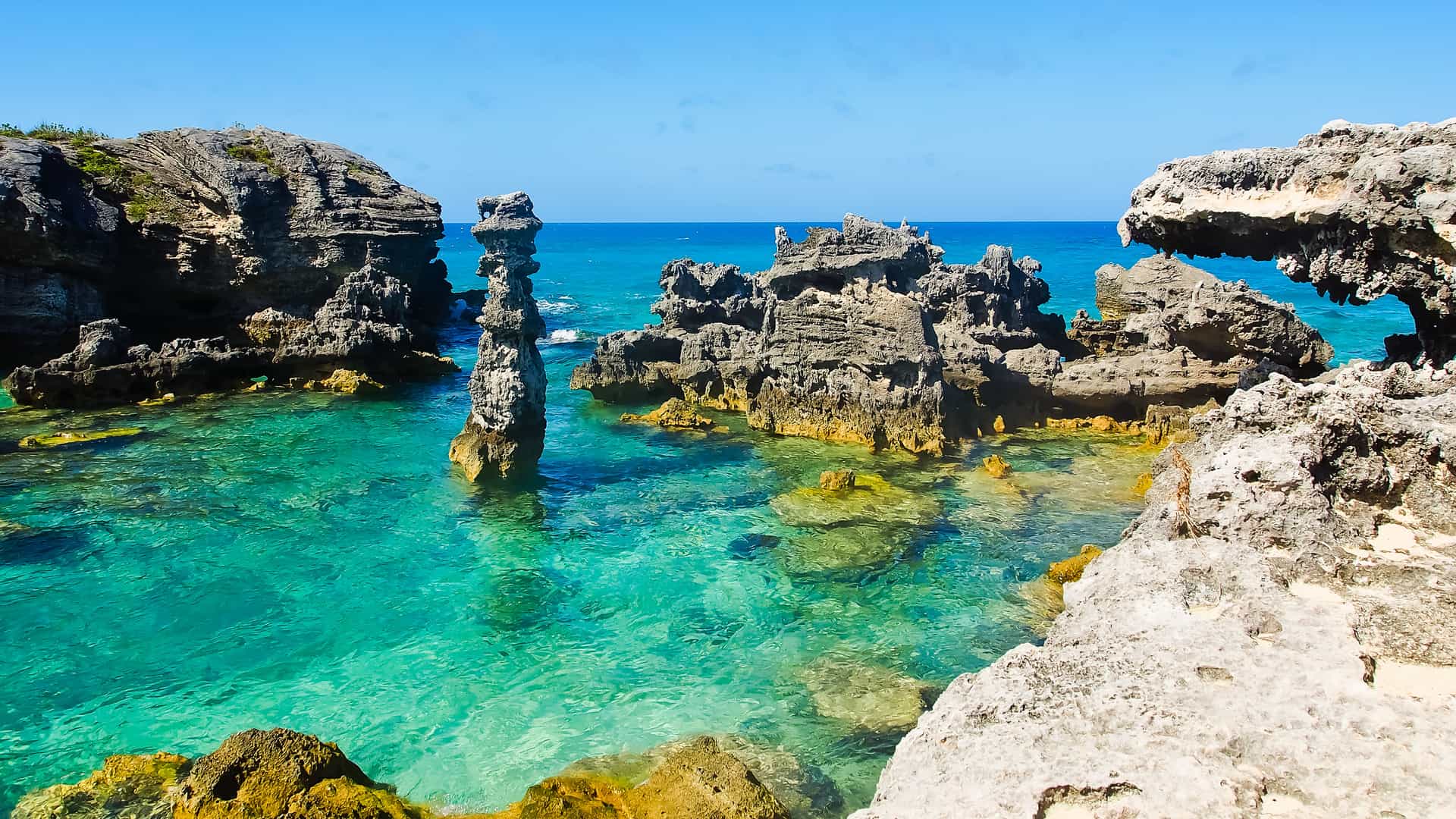 A large stone fortress, Fort St. Catherine, a historical landmark on the coast of St. George's, Bermuda, surrounded by lush green hills, trees, and turquoise water.