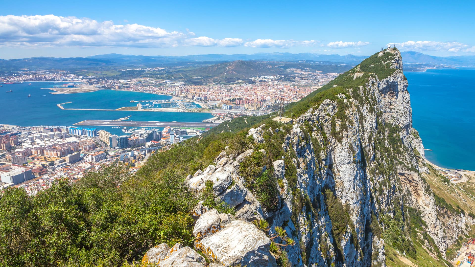 A breathtaking view of the Strait of Gibraltar from the Rock of Gibraltar, showing the bustling port and city below, with the deep blue sea in the distance.