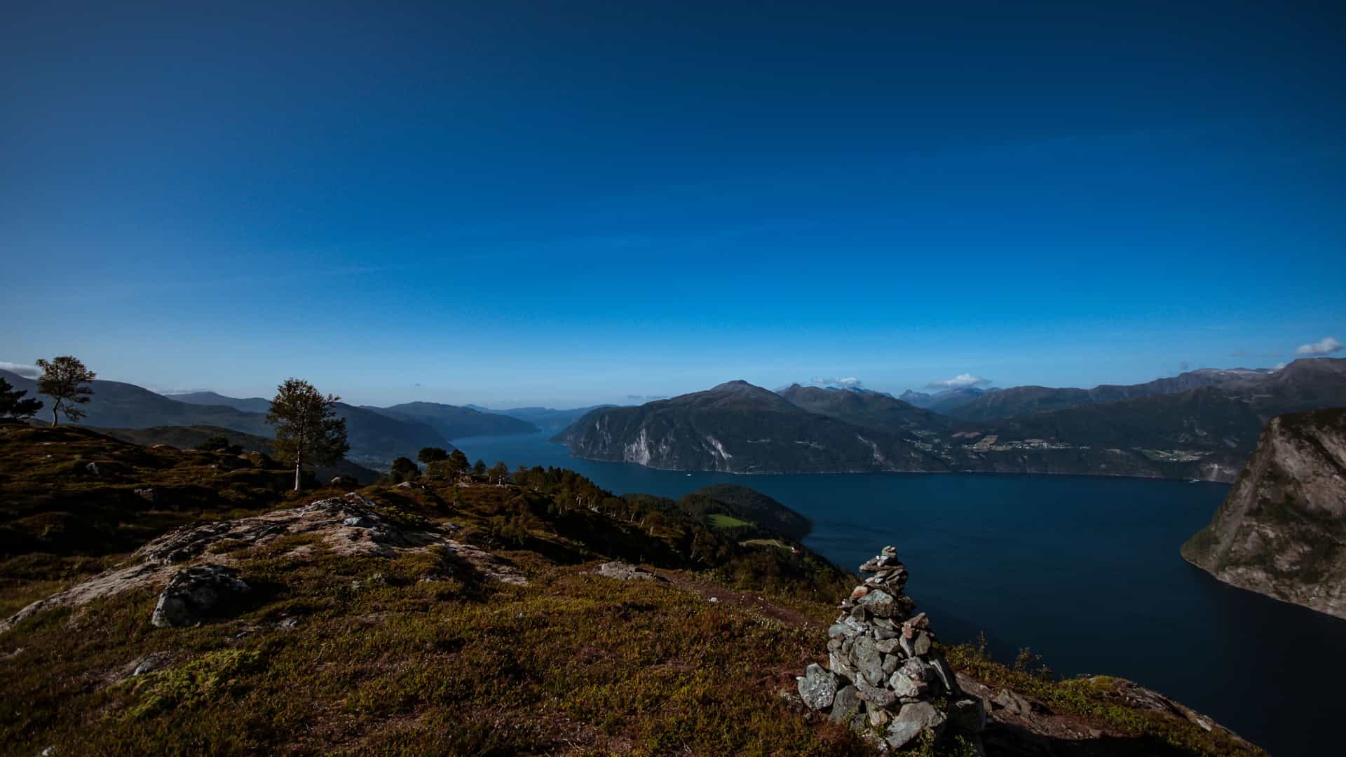 A breathtaking view from a rocky hilltop in Stranda, Norway, overlooking the scenic fjord and mountains under a clear blue sky.