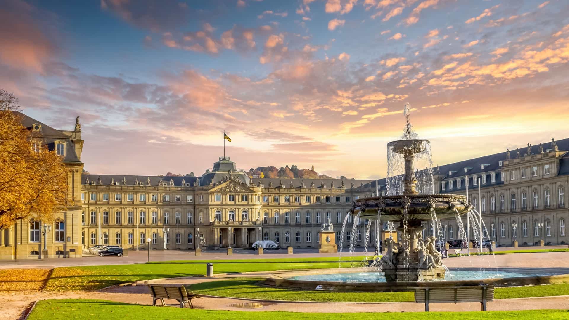 The baroque New Palace overlooks a public square with a grand fountain under a dramatic, cloudy sunset sky.
