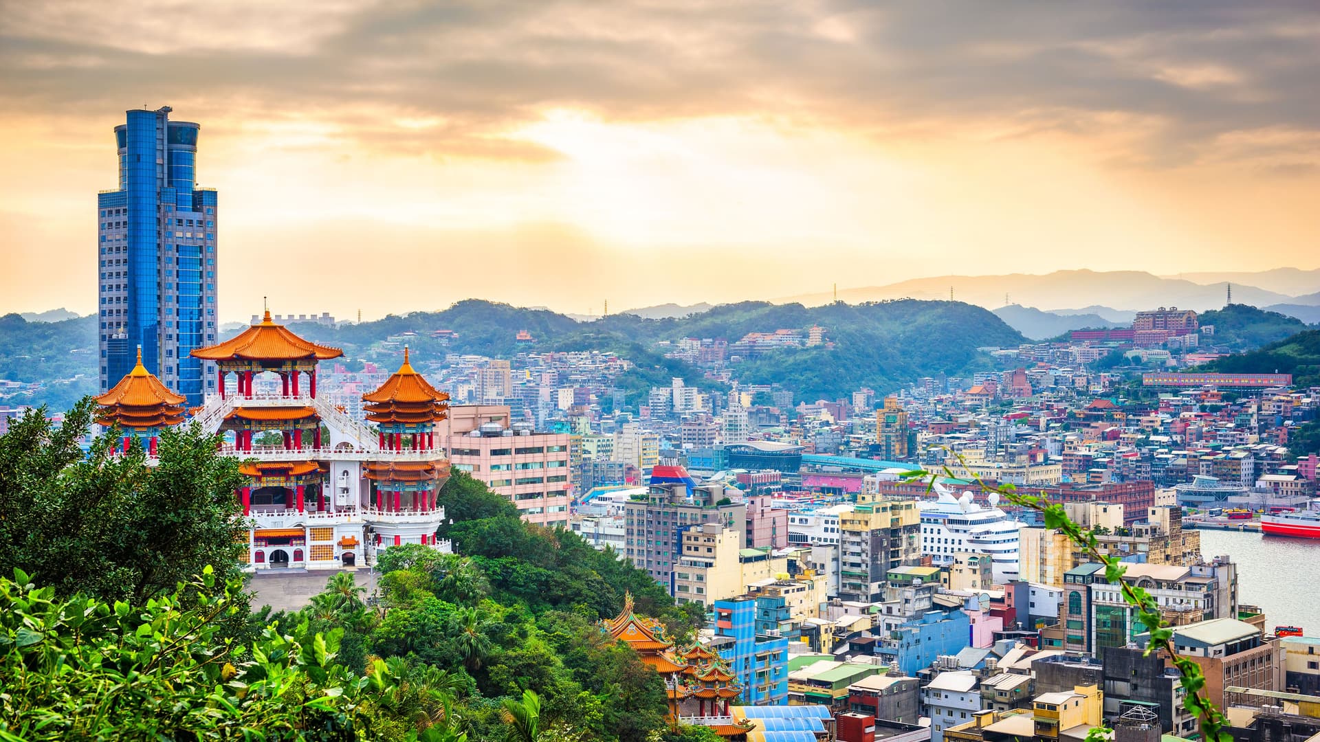 A beautiful panoramic view of the city of Keelung, Taiwan, with a large, ornate temple in the foreground and a busy port and colorful buildings in the background with mountains in the distance.