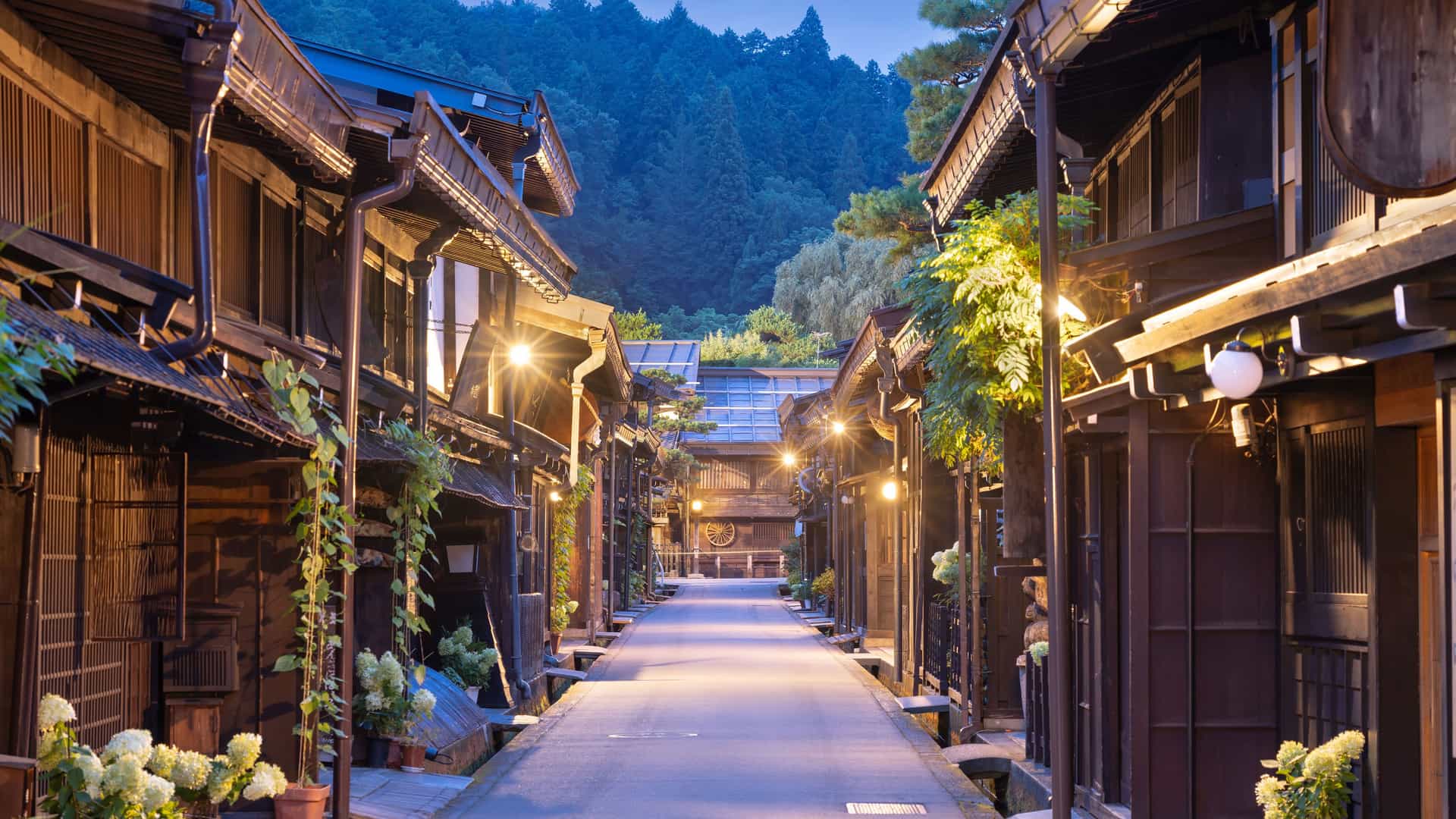 "A serene evening view of the historic district of Takayama, Japan, showing a narrow, empty street lined with traditional, dark wooden Japanese buildings and glowing lanterns. "