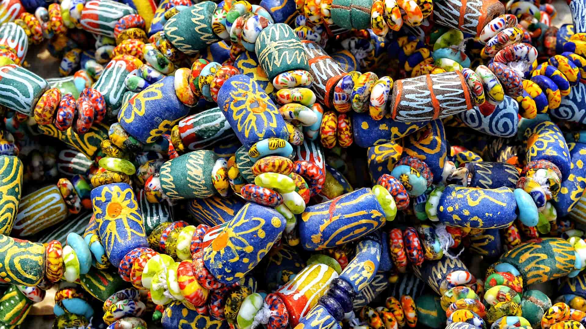 A close-up of a vibrant pile of handmade recycled glass beads, featuring intricate patterns and a variety of colorful designs from Takoradi, Ghana.