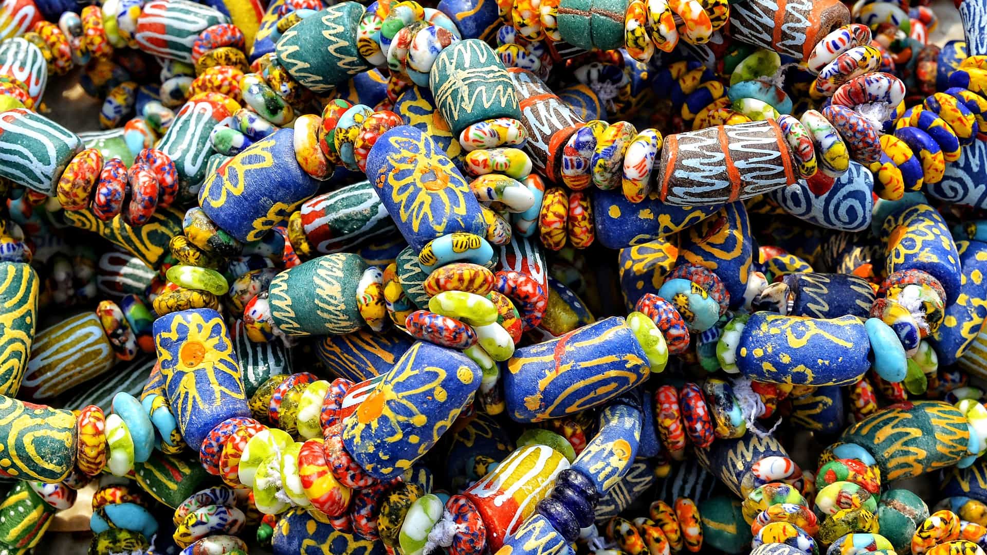 A close-up of a vibrant pile of handmade recycled glass beads, featuring intricate patterns and a variety of colorful designs from Takoradi, Ghana.