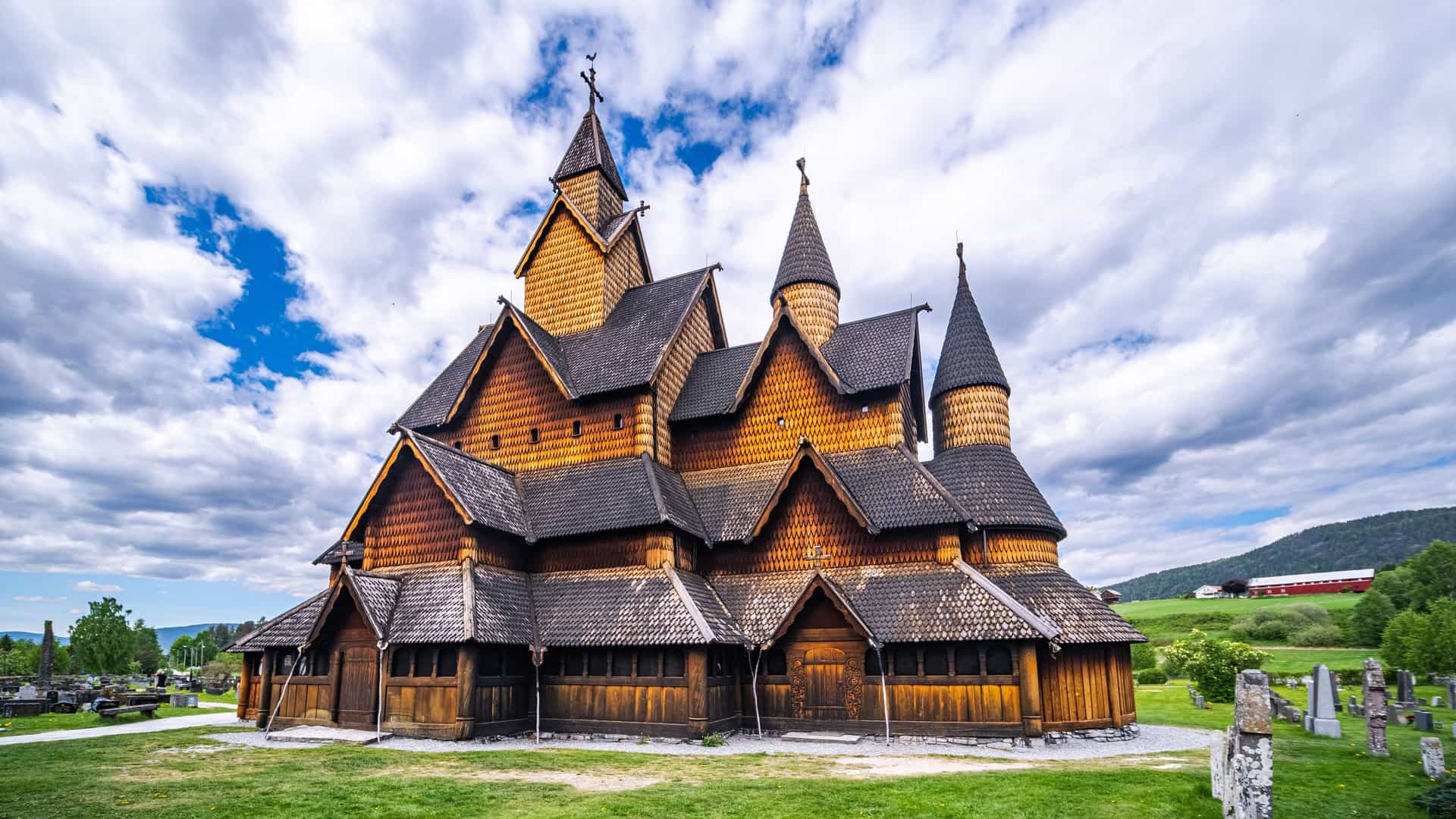 "A beautiful wide-angle shot of the medieval Heddal Stave Church, a unique and historic wooden structure with multiple roofs and spires, surrounded by a green lawn and a cemetery in Telemark, Norway. "