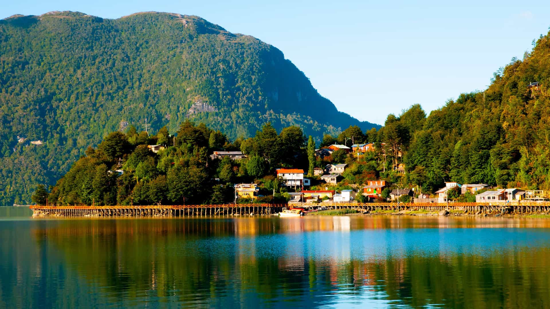 A serene view of the unique stilted houses and wooden boardwalks of Tortel, Chile, nestled on a forested mountainside along the Baker Channel.