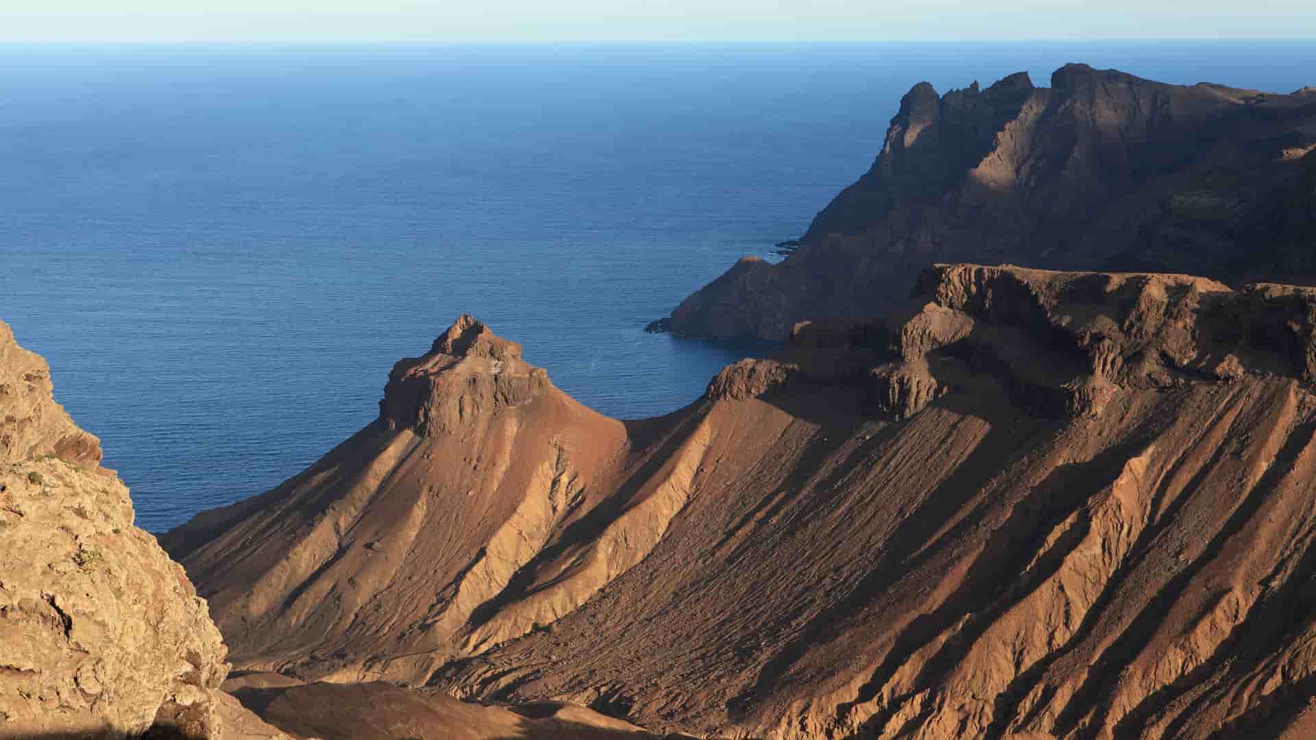 A high-angle view of the rugged, steep volcanic cliffs of Tristan da Cunha, the world's most remote inhabited archipelago, rising dramatically from the Atlantic Ocean.