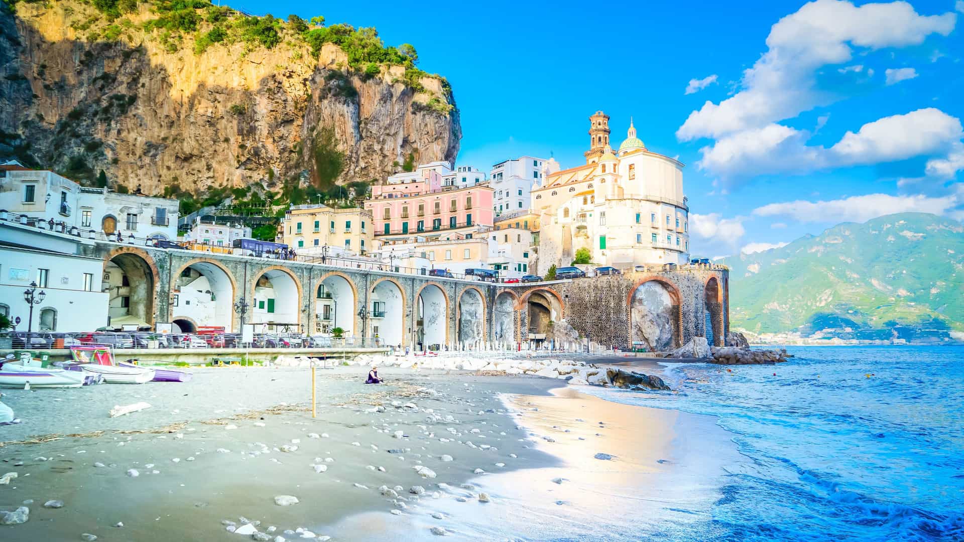 A scenic view of the coastal town of Atrani on the Tyrrhenian Sea, with pastel-colored houses and a church built into a cliffside on Italy's Amalfi Coast.