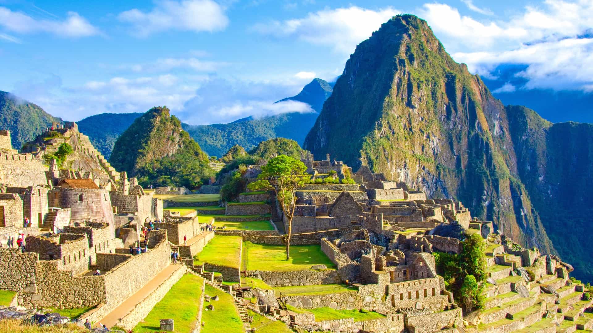 An awe-inspiring view of the ancient Incan citadel of Machu Picchu, with its stone terraces and structures set against the dramatic, lush green mountains in the Urubamba Valley of Peru.