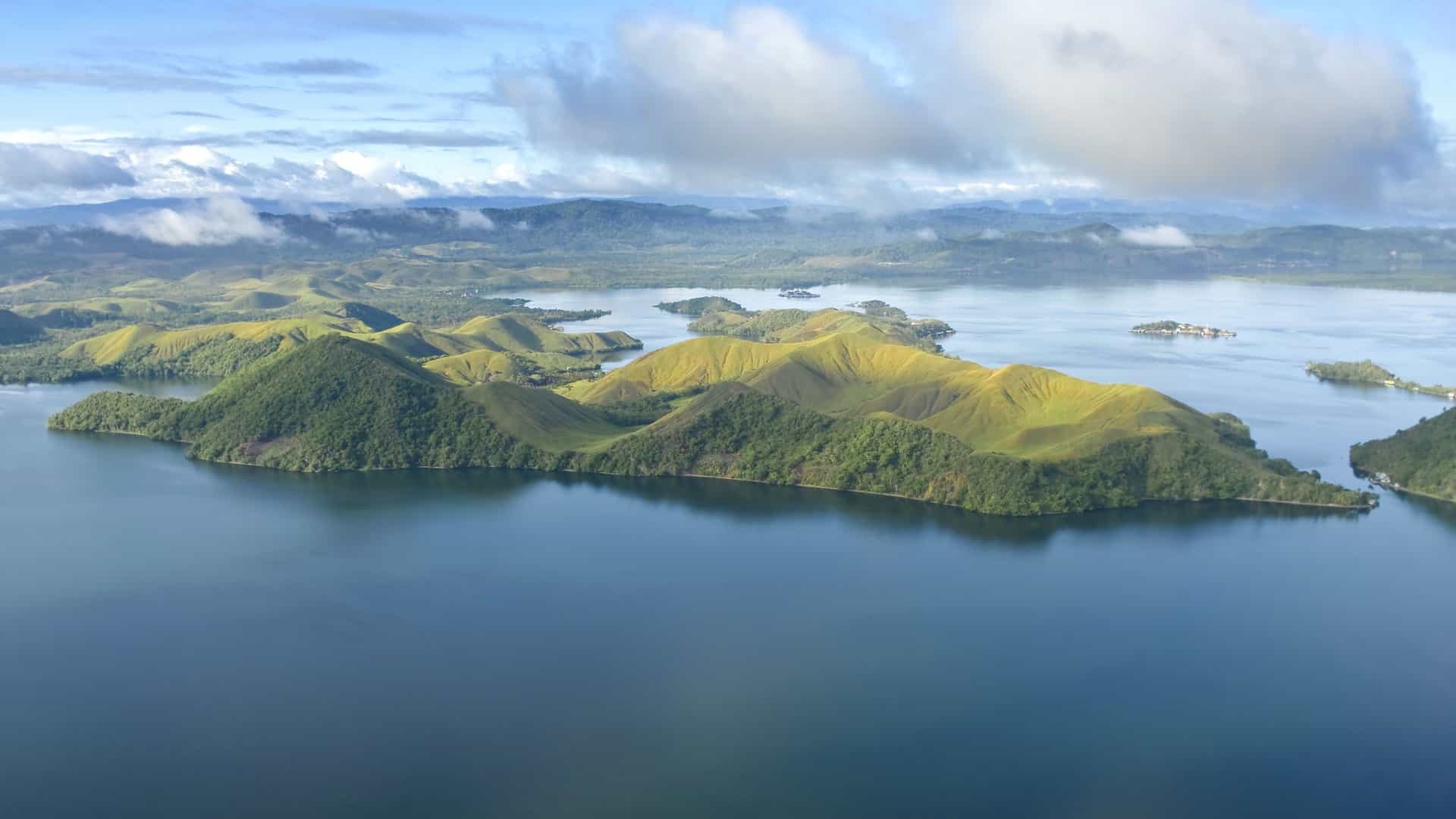 An aerial view of the verdant, rolling hills and a peninsula jutting out into the deep blue waters of Vanimo, a picturesque coastal town in Papua New Guinea.
