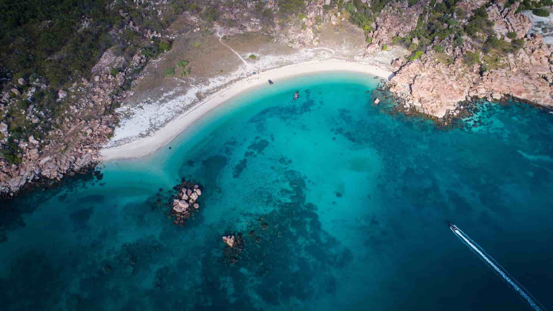 An aerial drone shot of Vansittart Bay, with a speed boat cutting through the deep turquoise water as it approaches a secluded beach in Western Australia.