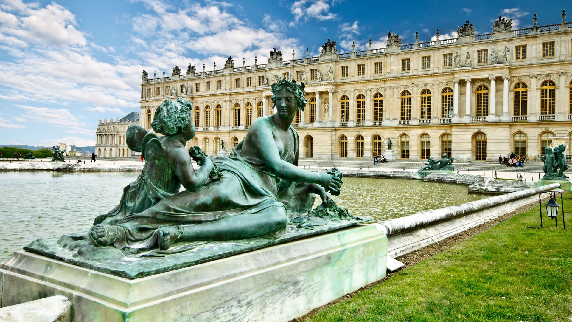A beautiful view of a large bronze statue of two figures on the shore of a pond in the gardens of the magnificent Palace of Versailles, a UNESCO World Heritage Site near Paris.