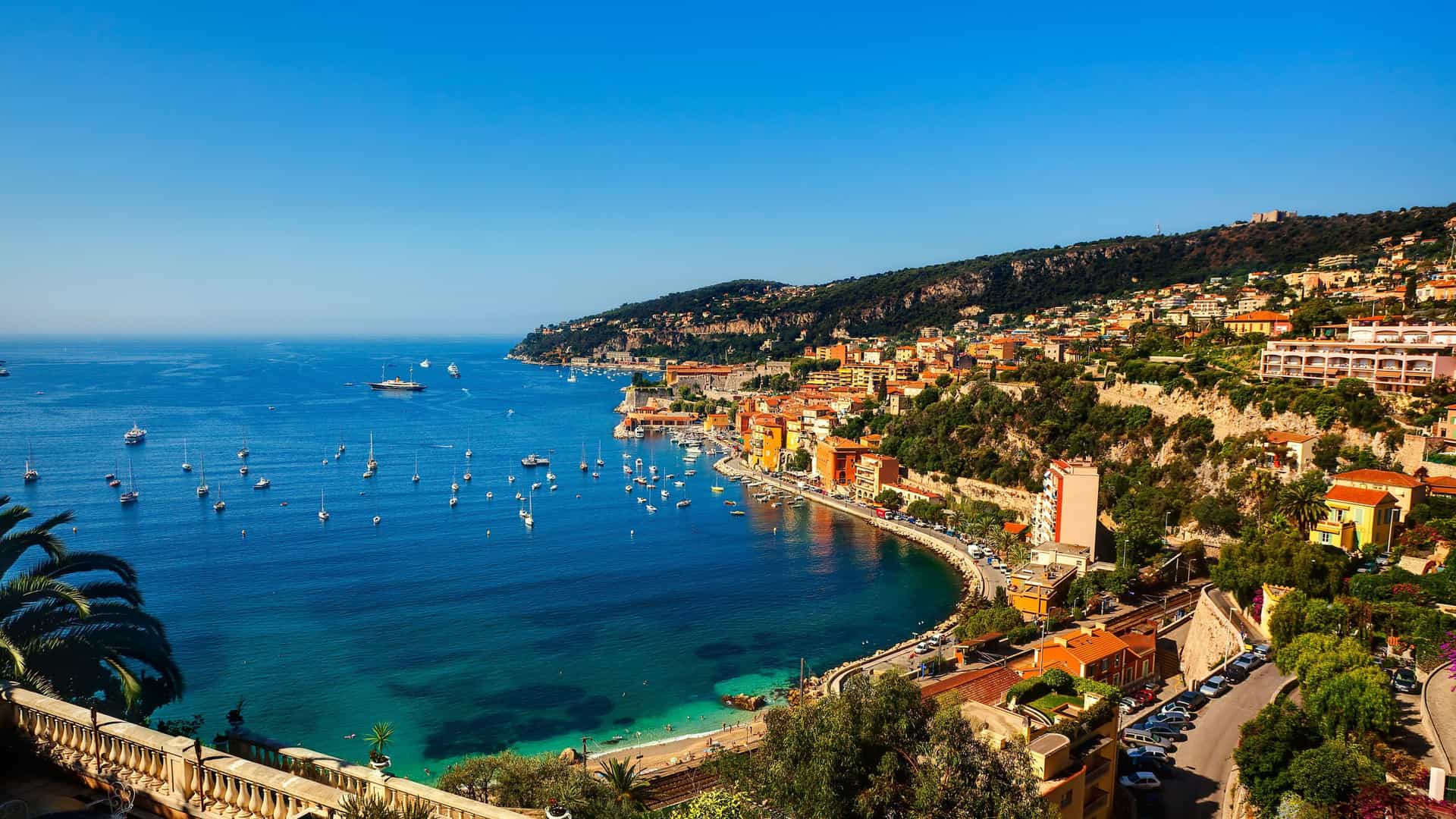 A beautiful panoramic view of the colorful houses and yachts in the bay of Villefranche-sur-Saône, France, with lush, green hills in the background.