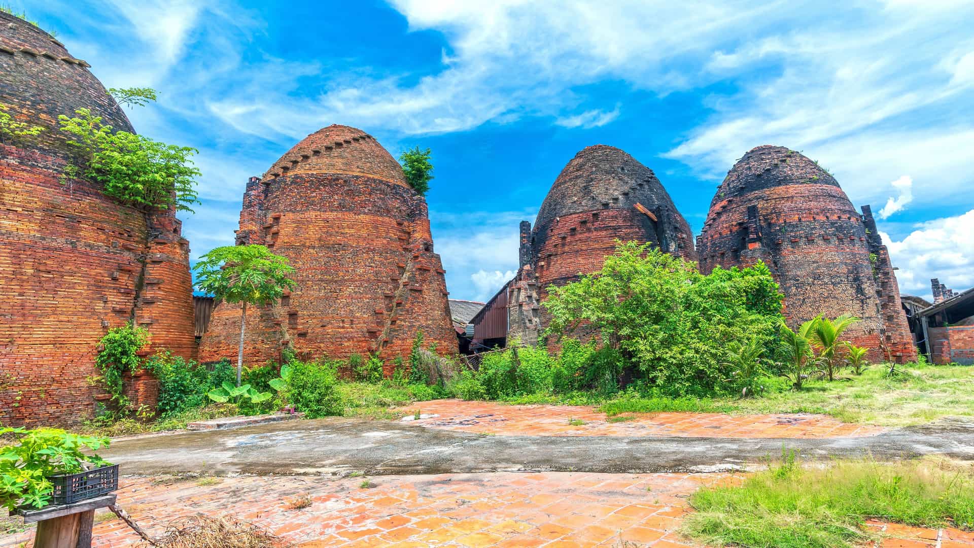 A scenic view of the traditional brick kilns of the Mang Thit brick factory in Vinh Long, Vietnam, with a blue sky and white clouds in the background.
