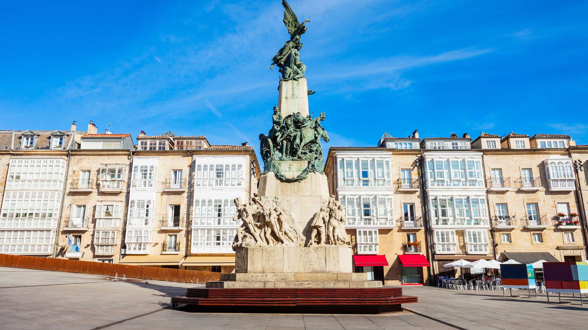 "A bronze monument of a winged figure on horseback atop a stone base, standing in the center of a wide city square with historic buildings in Vitoria-Gasteiz, Spain. "