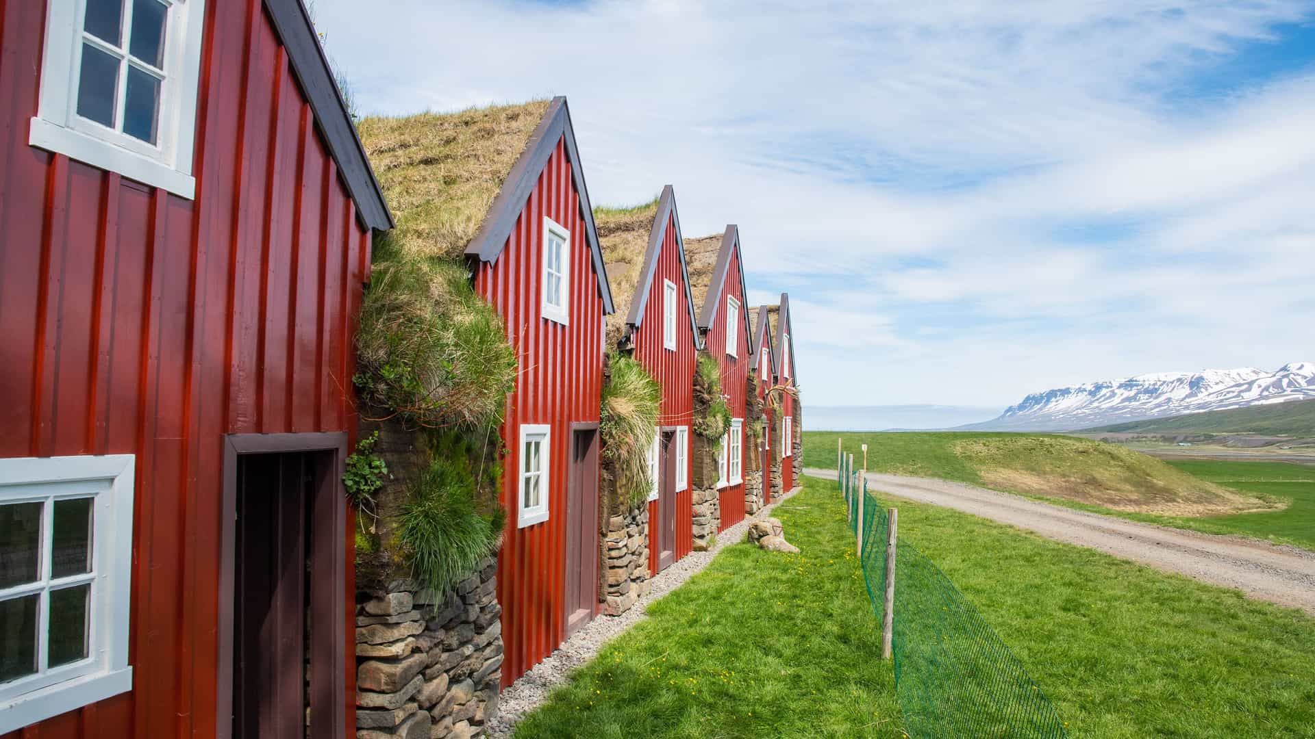 A beautiful row of red, traditional Icelandic turf houses with grass roofs, located next to a dirt road in the picturesque countryside of Vopnafjordur, Iceland.