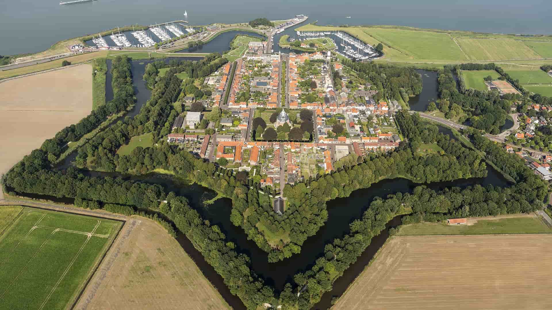 "An aerial view of the historic star-shaped fortress town of Willemstad, the Netherlands, surrounded by a moat and lush green fields. "