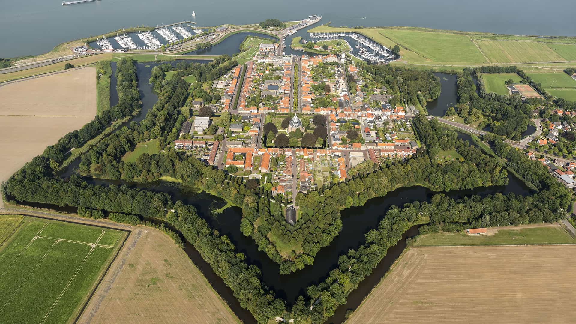 "An aerial view of the historic star-shaped fortress town of Willemstad, the Netherlands, surrounded by a moat and lush green fields. "