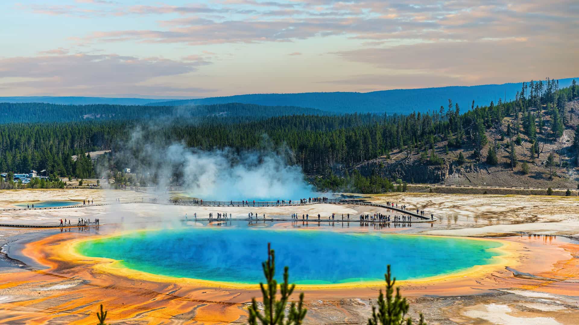 "A vibrant aerial shot of the Grand Prismatic Spring in Yellowstone National Park, Wyoming, with its stunning, multi-colored bacterial mats and steam rising from the hot spring."