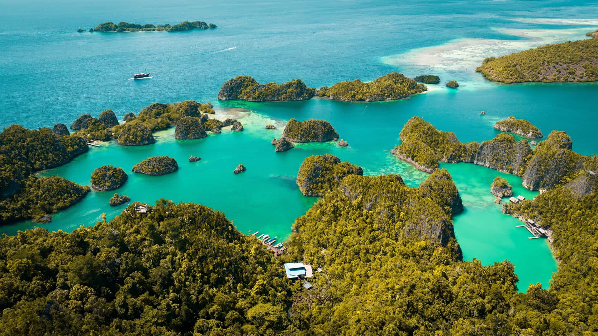 An aerial shot of the exotic Wayag Islands in Raja Ampat, Indonesia, with stunning karst formations covered in green vegetation surrounded by beautiful turquoise water.