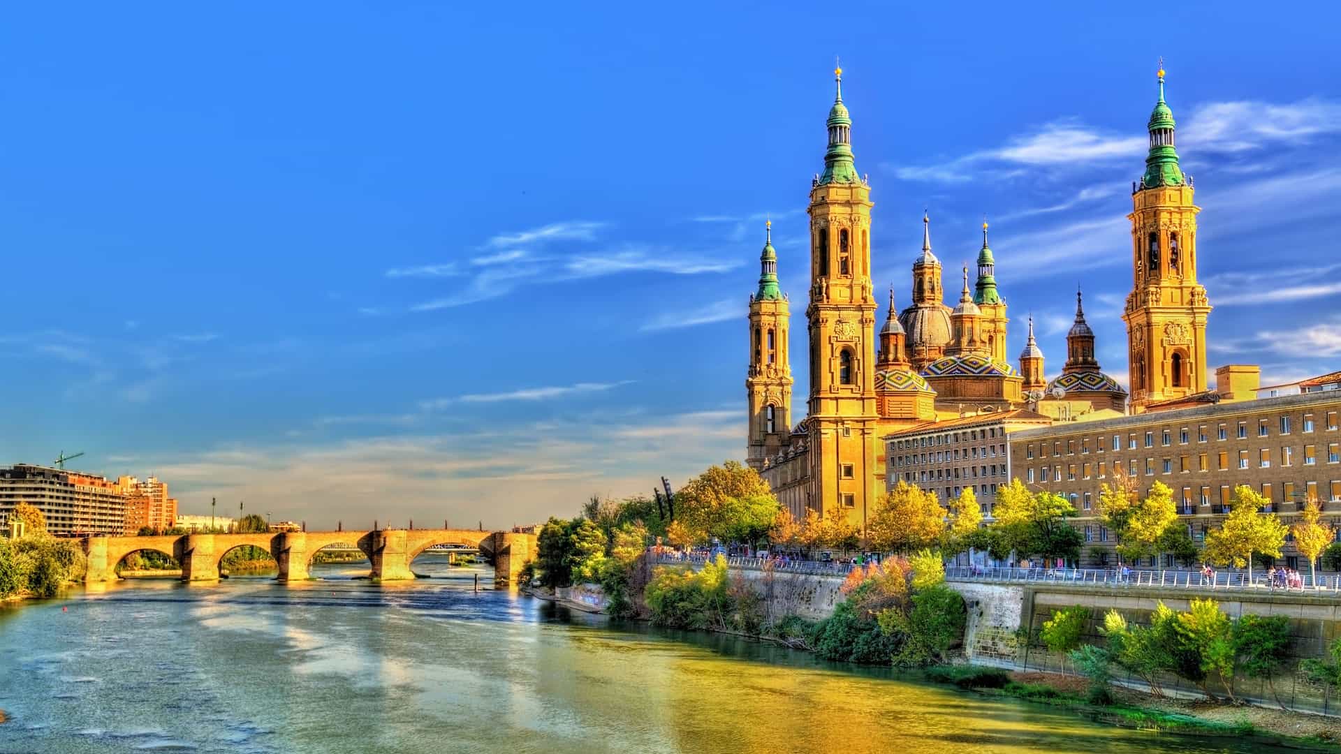 "A vibrant sunset over the Ebro River in Zaragoza, Spain, with the iconic Basilica de Nuestra Señora del Pilar and the medieval Puente de Piedra bridge in the background."