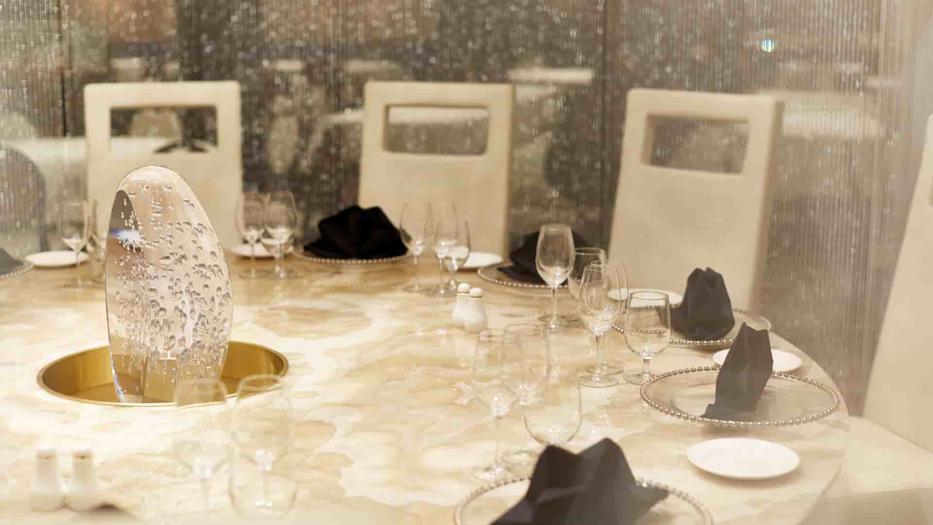 A close-up view of an elegant round dining table set with pristine place settings, black napkins, and a glowing bubble-glass centerpiece, surrounded by shimmering silver beaded curtains.