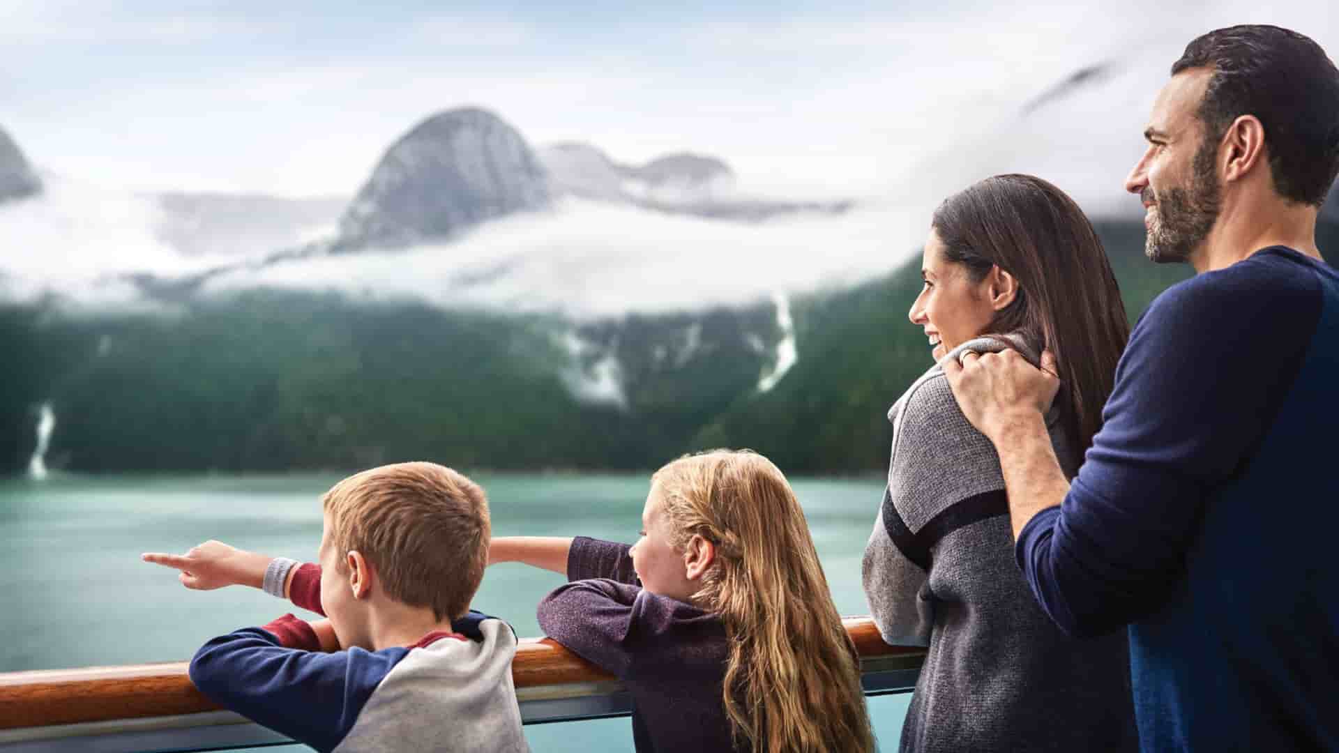 A family of four looks out from a cruise ship deck at the scenic, misty mountains during an Alaska family cruise on Princess Cruises.