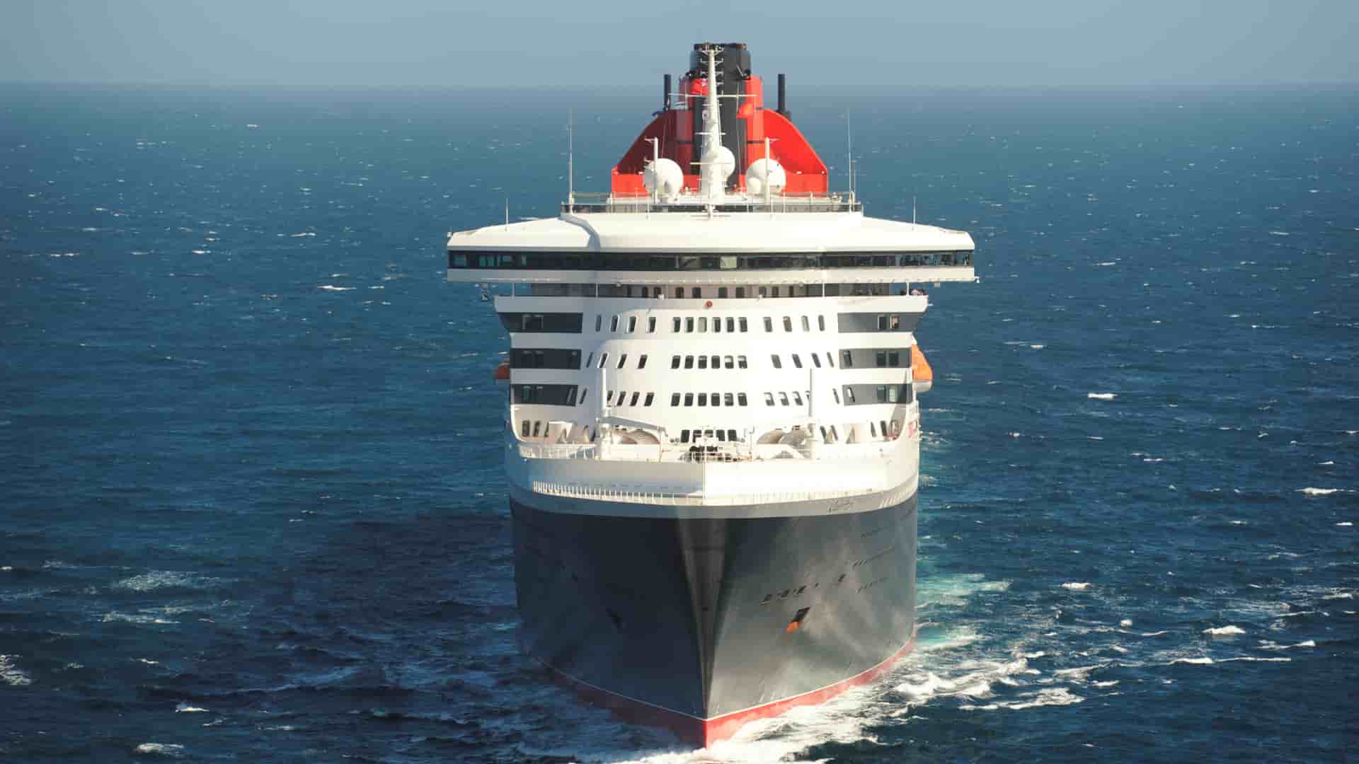 Front-facing view of the iconic Cunard ocean liner Queen Mary 2 navigating through the open blue ocean.