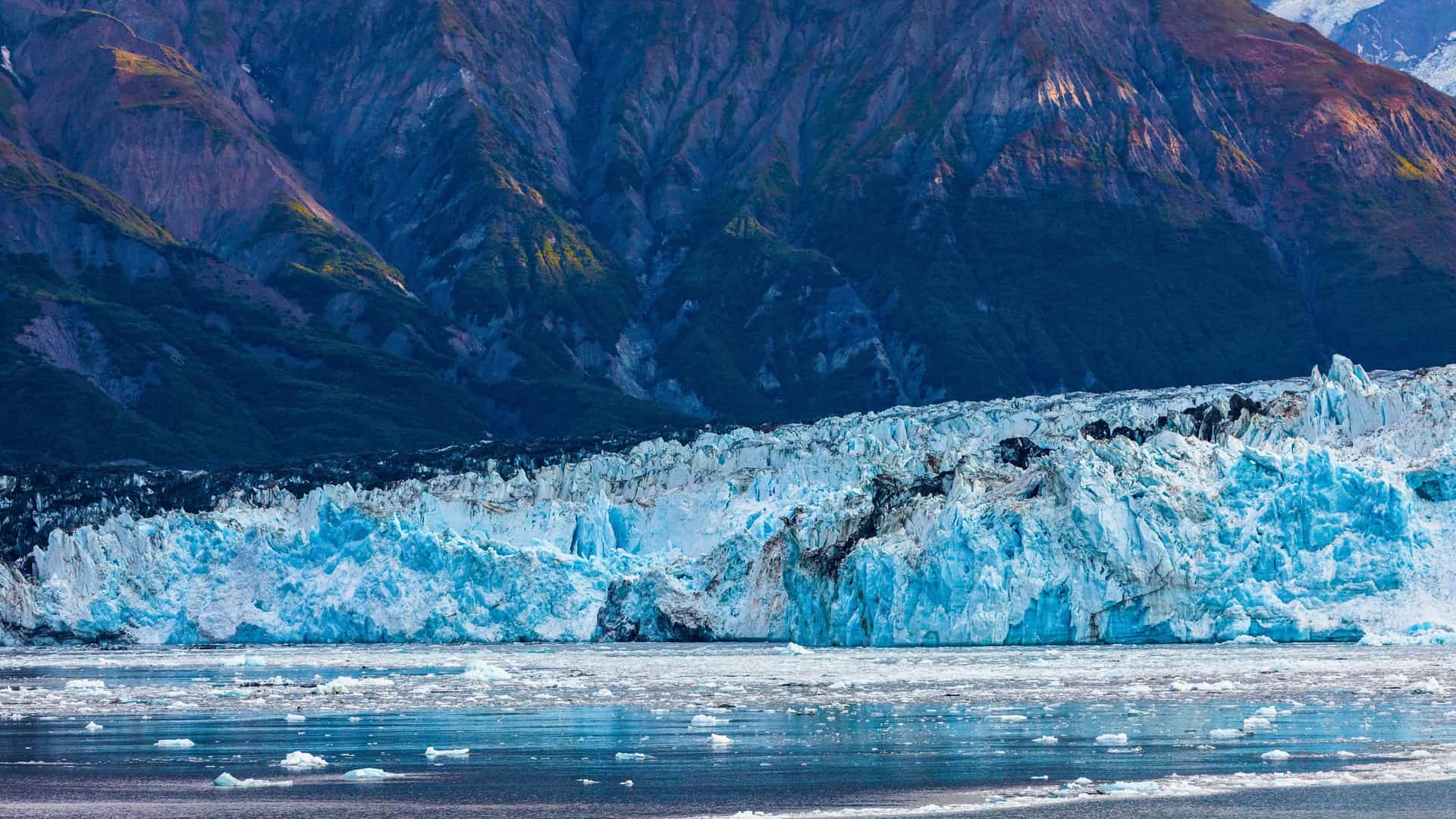 Regent Seven Seas cruise ship sailing past the stunning Hubbard Glacier in Alaska, with icebergs floating in the frigid water.