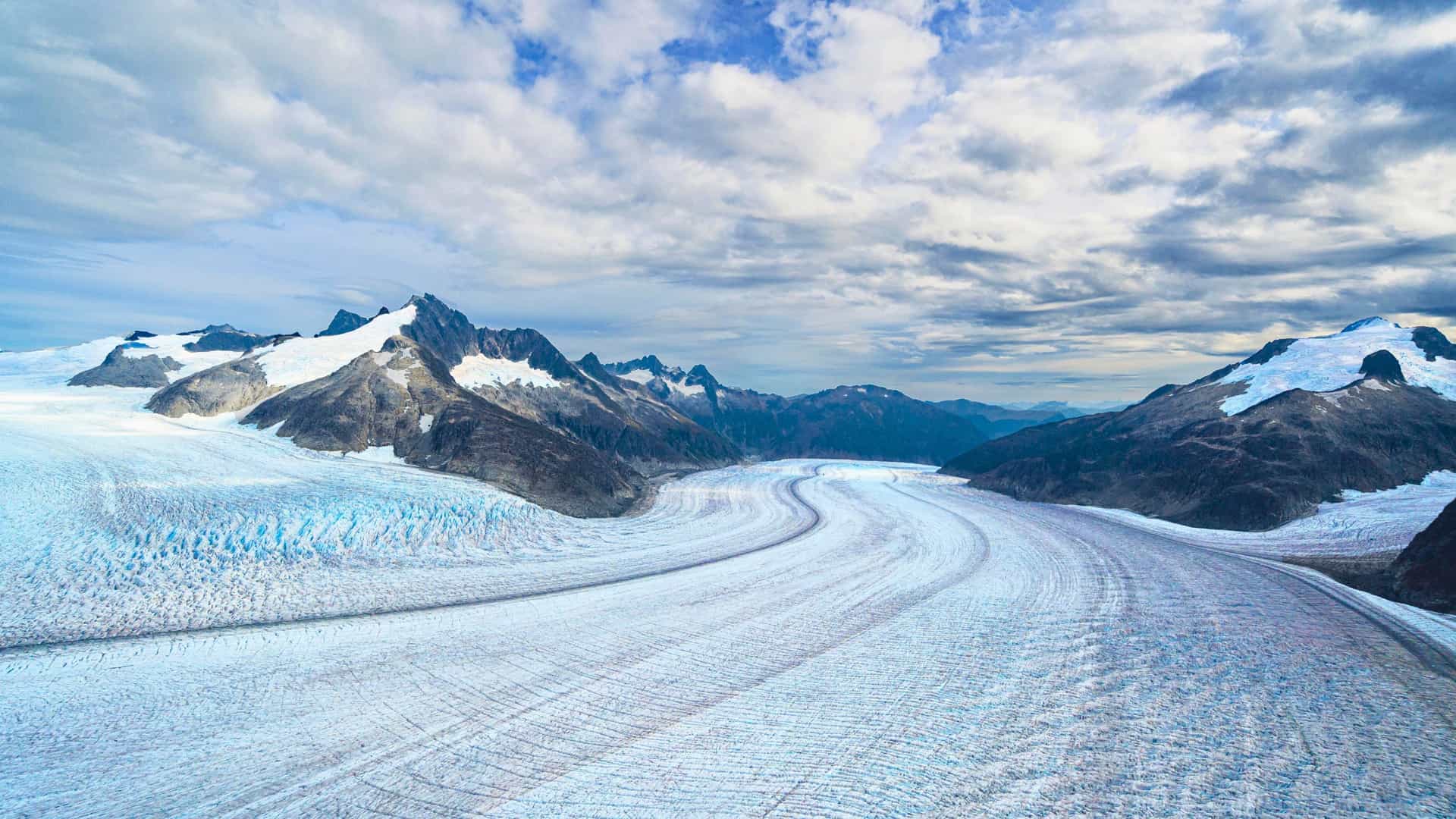 An aerial view of a massive glacier winding through the mountains of Juneau, Alaska, a stunning landscape to be experienced on a Royal Caribbean cruise.