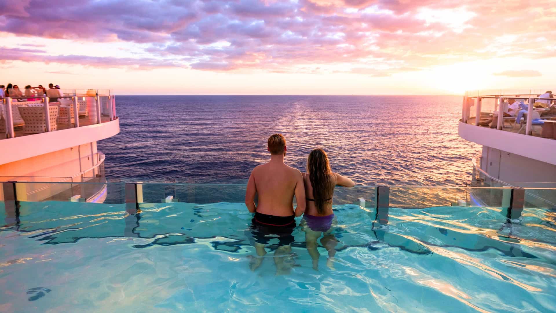 A couple enjoys the sunset from a pool on a Royal Caribbean cruise ship during a Trans-Pacific voyage across the vast ocean.