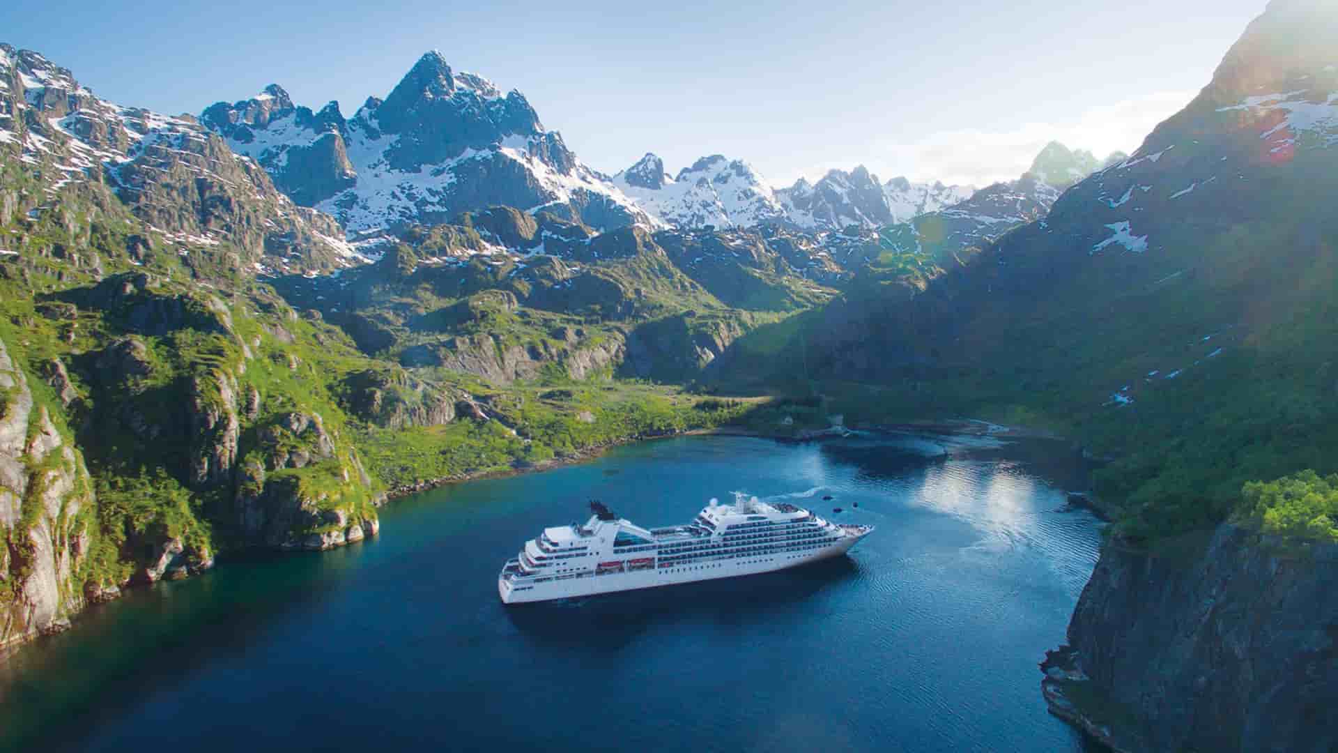 A luxury Seabourn cruise ship sails through a majestic Norwegian fjord, surrounded by towering mountains and serene waters.