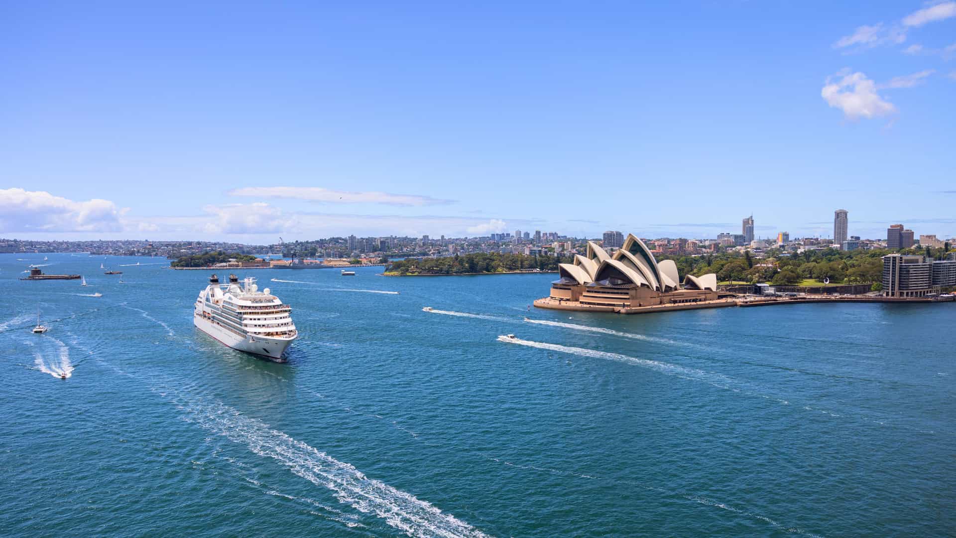 A luxurious Seabourn cruise ship sailing in Sydney Harbour with the iconic Sydney Opera House in the background, a highlight of an Australia and New Zealand itinerary.