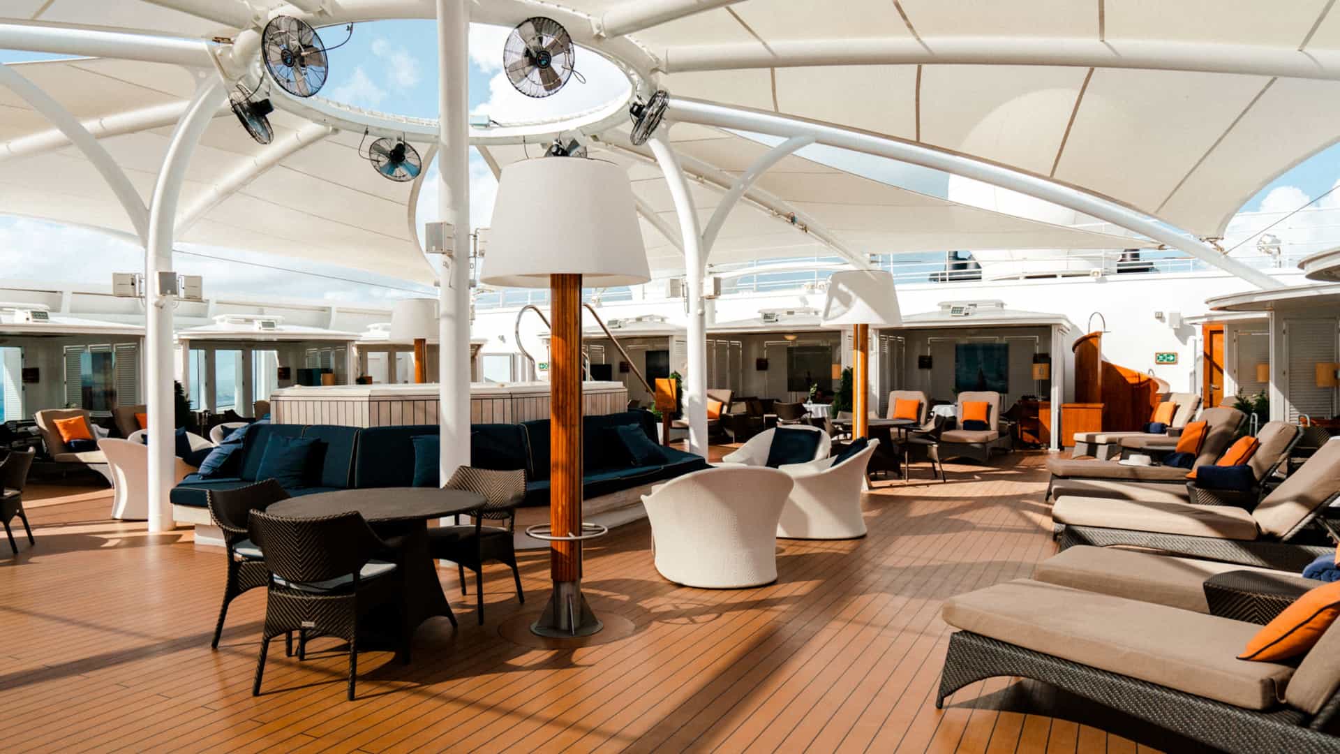 The Retreat outdoor lounge area on a Seabourn cruise ship featuring cushioned sun loungers, private cabanas, a central whirlpool area under a white tented canopy, and wooden decking.