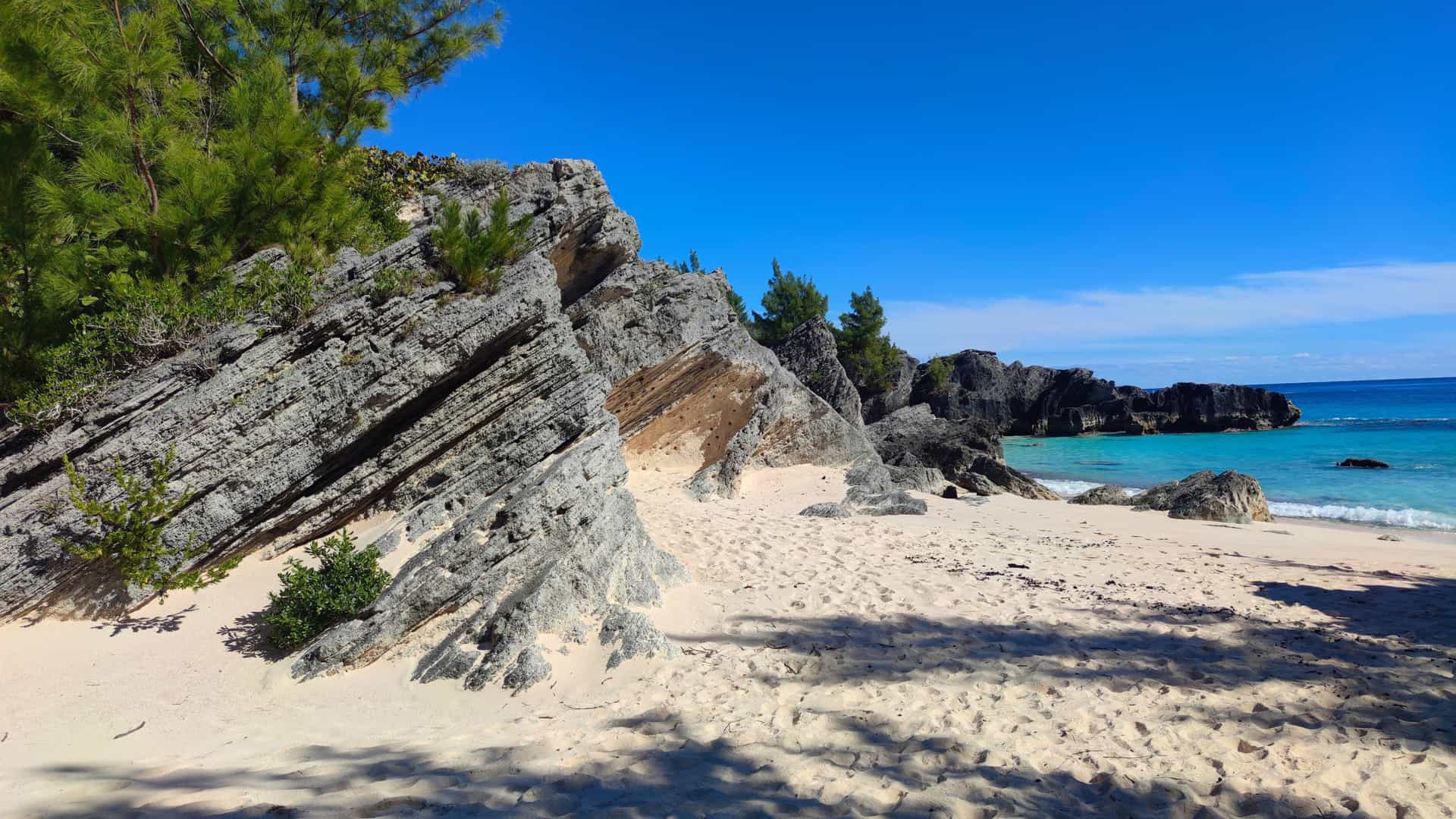 A scenic beach with white sand, turquoise water, and jagged rock formations under a clear blue sky in Bermuda, a destination on a Silversea cruise.