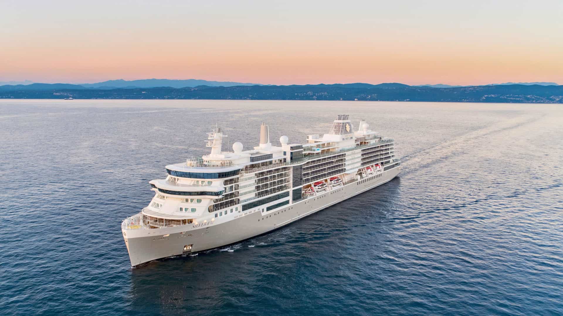 A Silversea cruise ship sailing on the open ocean during a Trans-Atlantic voyage at dawn or dusk.