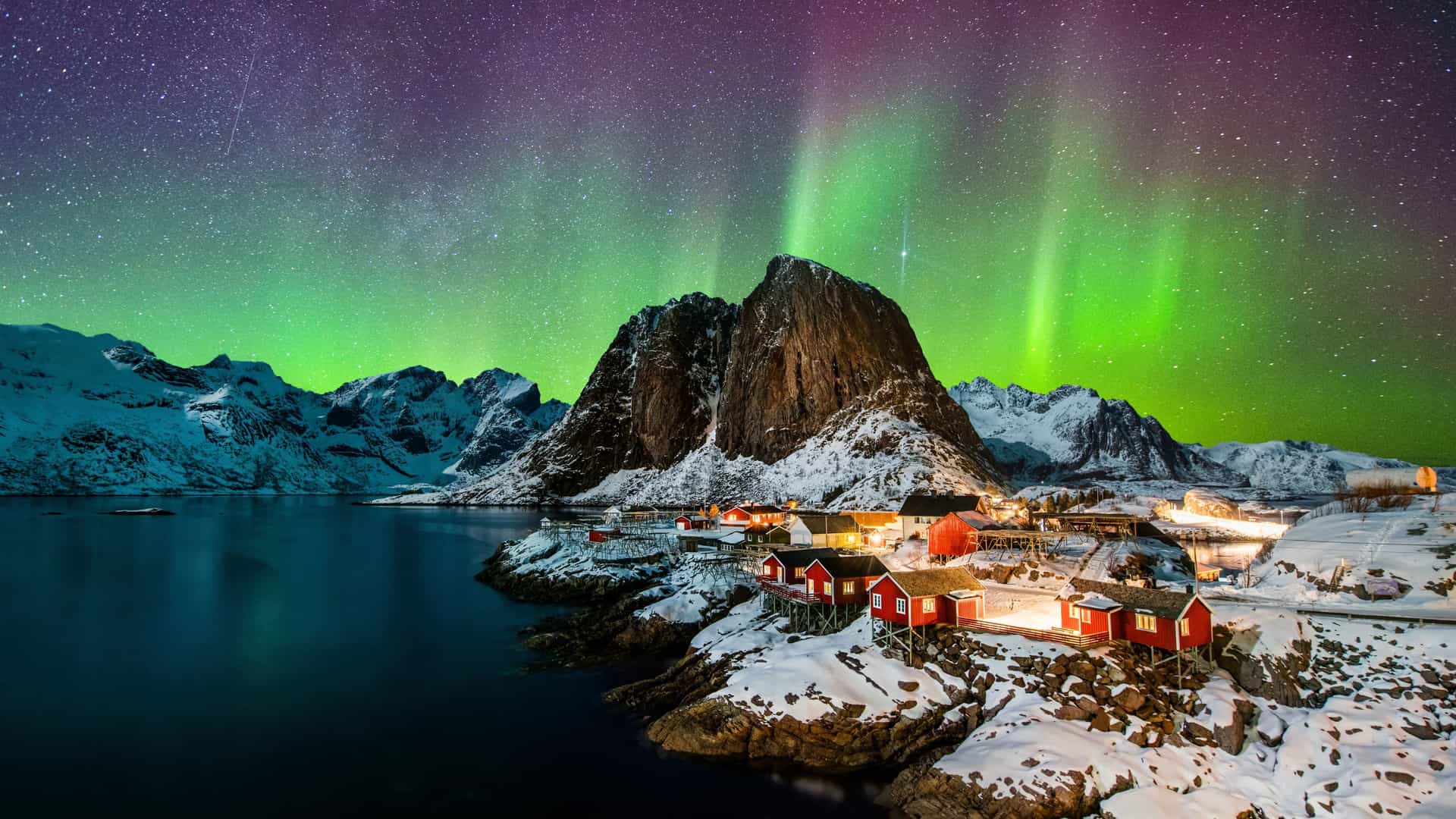 Vibrant green Northern Lights lighting up the night sky over a snow-covered fishing village and fjord on a Tauck Arctic Circle cruise.