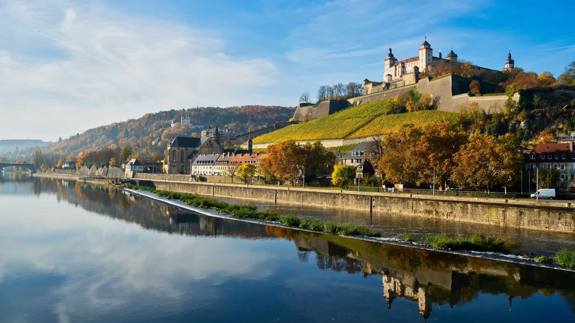 Scenic view of a historic fortress on a hill overlooking a calm river, terraced vineyards, and autumn trees on a Tauck river cruise.