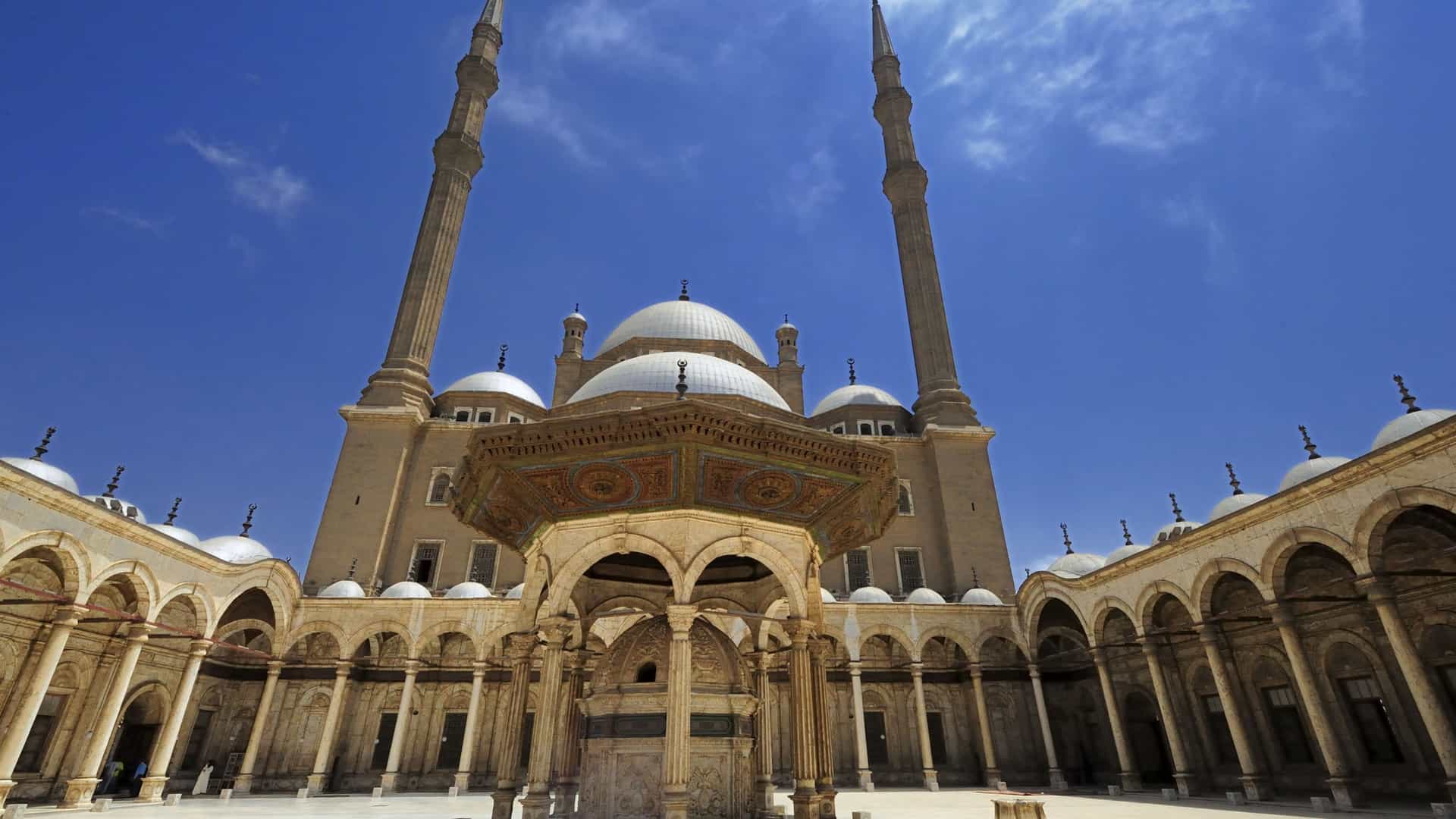 Grand courtyard featuring tall minarets, large domes, and ornate stone arches of a historic mosque on a Tauck Middle East tour.