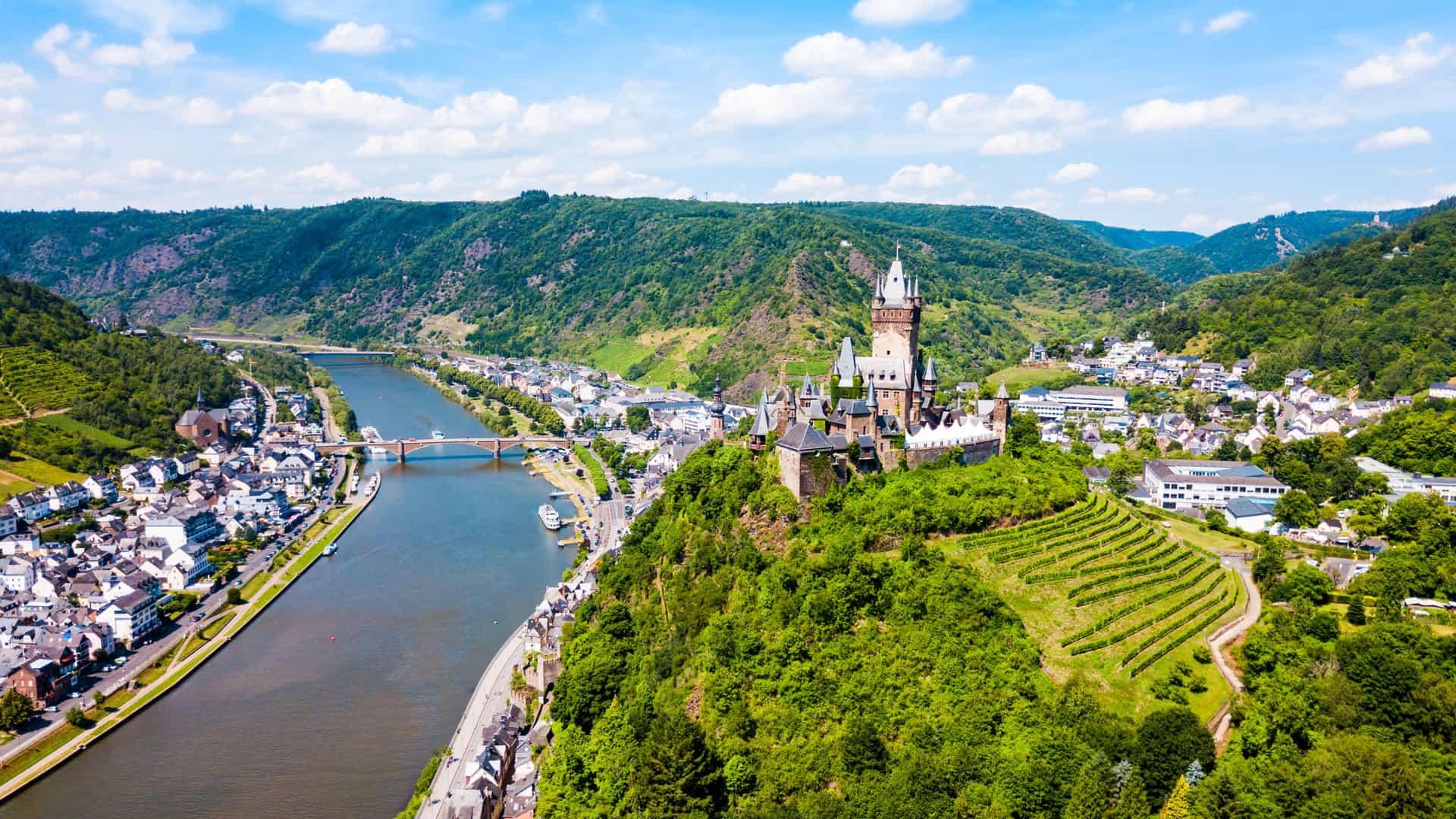 Scenic view of a majestic medieval castle perched on a wooded hill overlooking the winding Moselle River and historic town on a Tauck river cruise.
