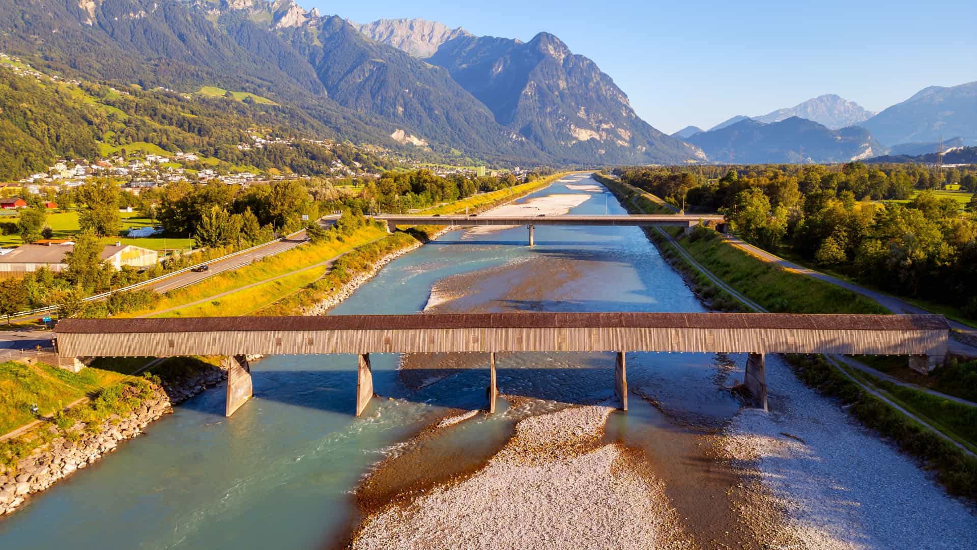 Scenic view of a traditional covered wooden bridge spanning the Alpine Rhine River with dramatic mountains in the background on a Tauck river cruise.
