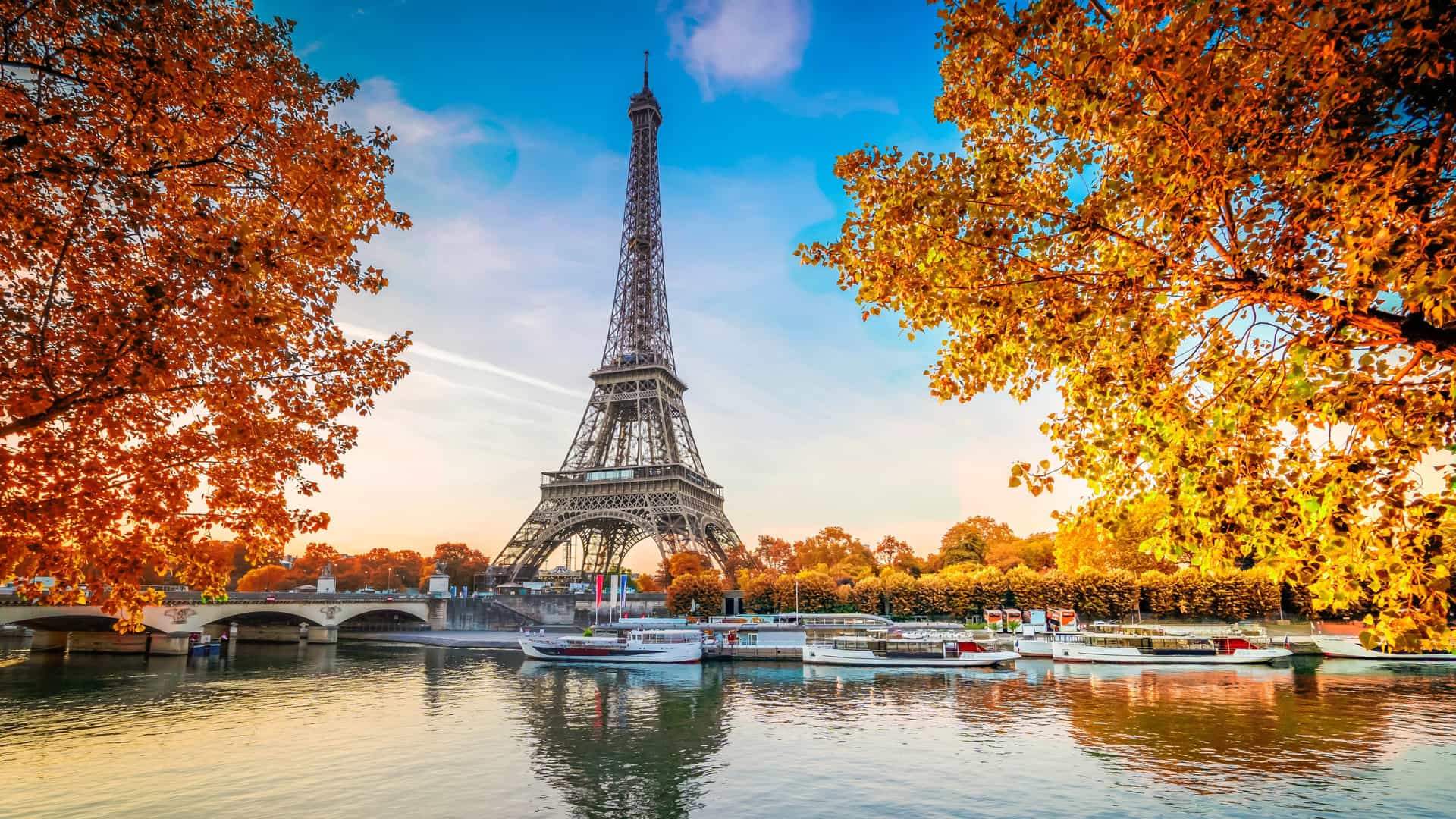 Scenic view of the Eiffel Tower framed by autumn trees along the Seine River with tour boats docked in Paris on a Tauck river cruise.