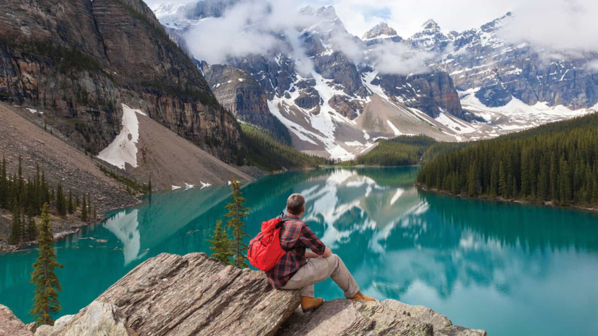 A hiker sitting on a cliff overlooking a bright turquoise lake in the heart of the Canadian Rockies during a Tauck tour.