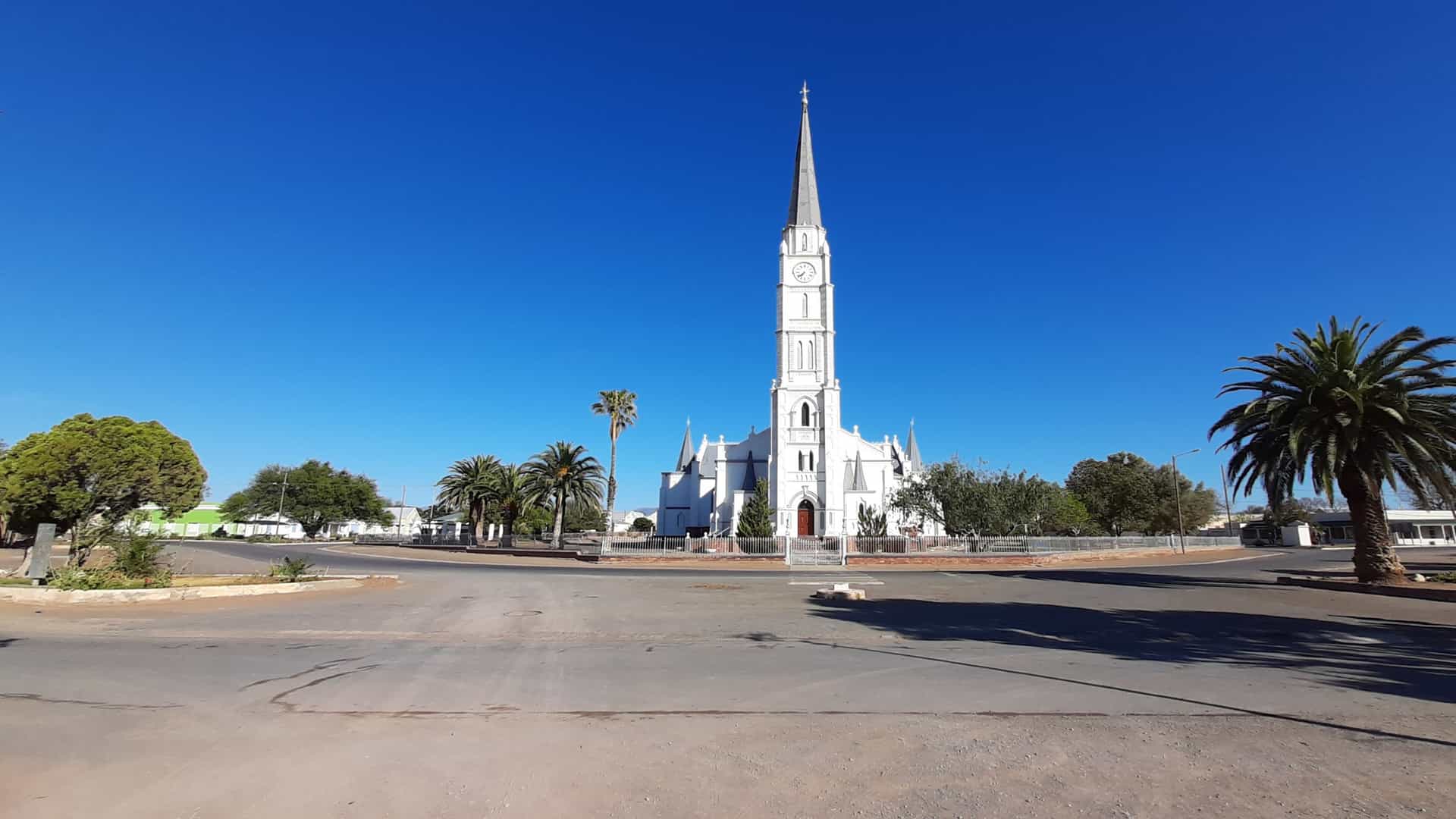 A bright view of Aberdeen in Freetown, Sierra Leone, featuring a white Gothic‑style church with a tall steeple, palm‑lined roads, and an open town intersection under a clear blue sky.